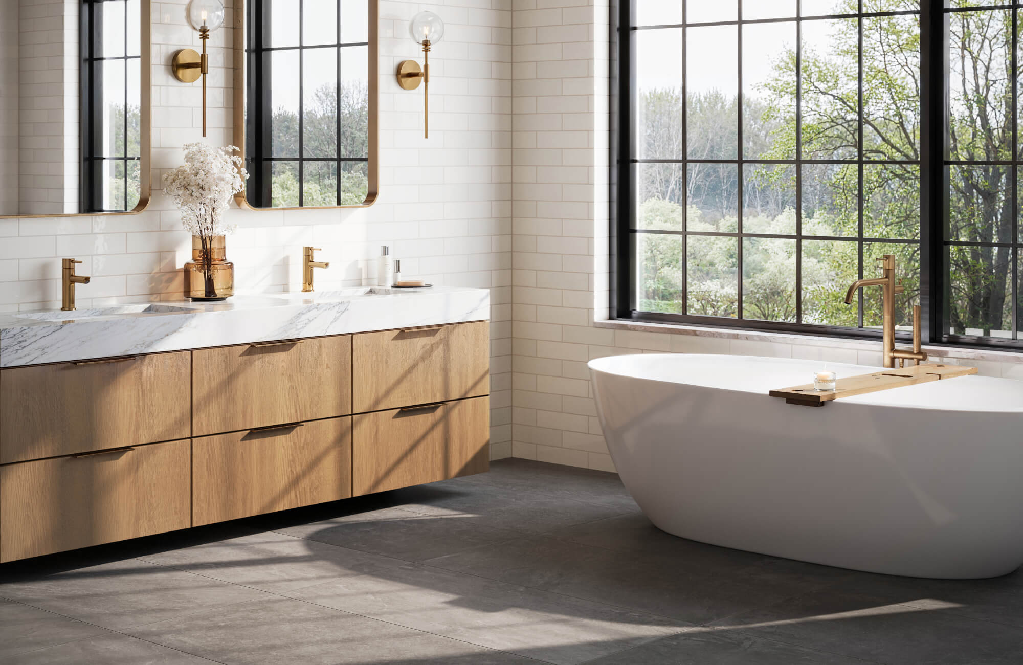 Contemporary bathroom with white subway tile walls, dark gray stone floor, oak vanity, freestanding tub, and brass fixtures.