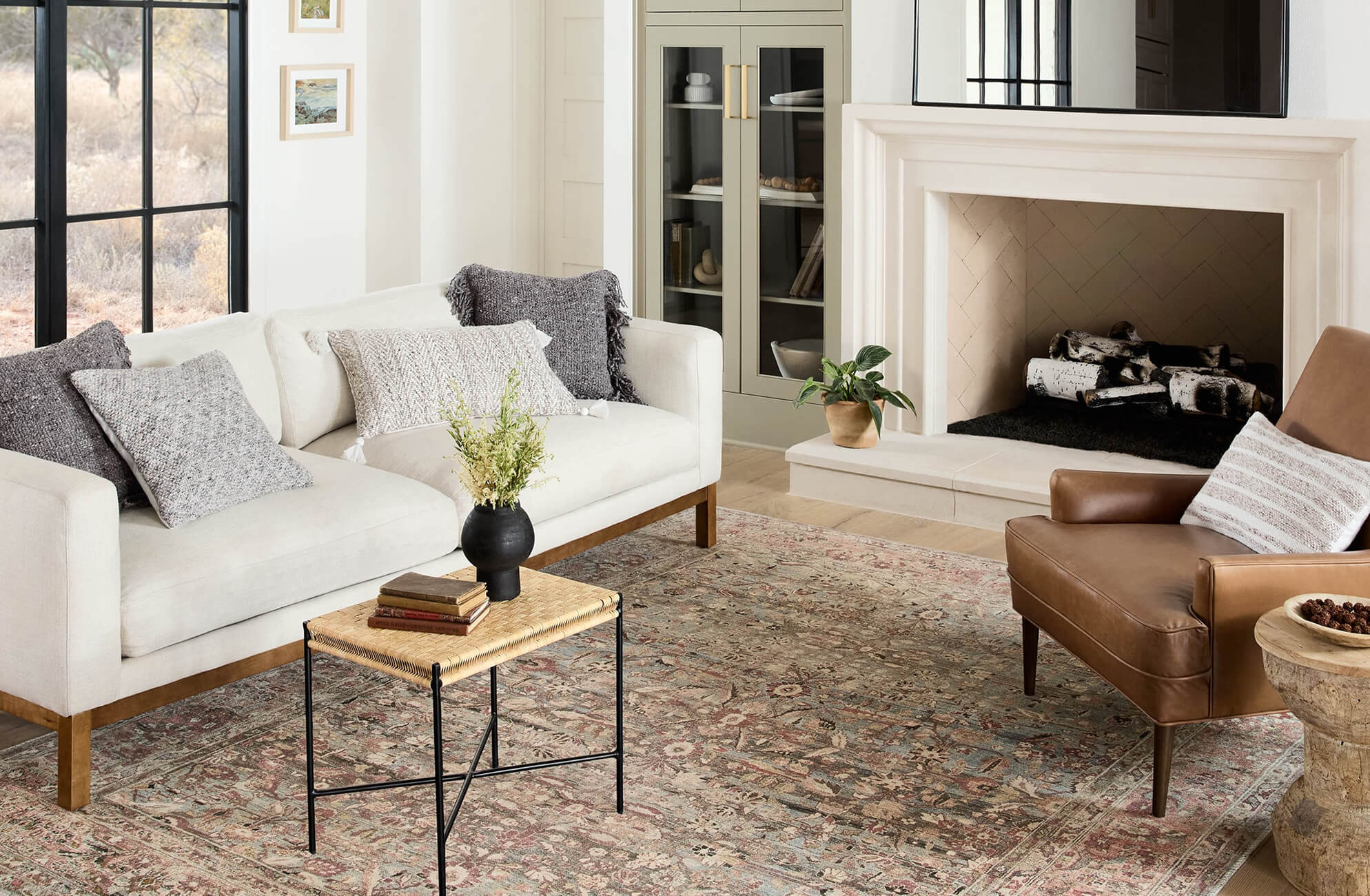 Ivory-toned sofa and rich brown leather chair atop a faded power loomed vintage-style rug in earthy reds, blues, and taupe.