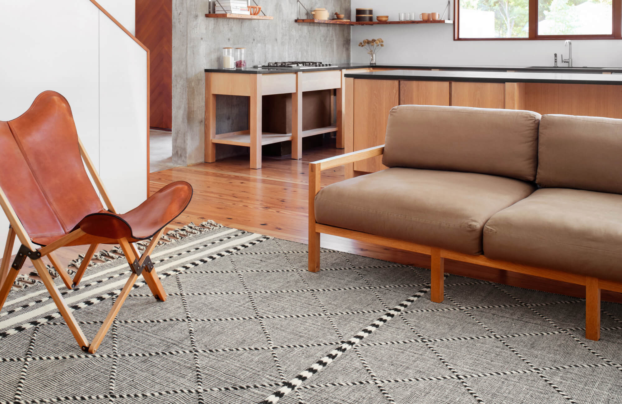 Warm taupe sofa paired with a cognac leather chair, set on a gray diamond-patterned rug with black and white accents.