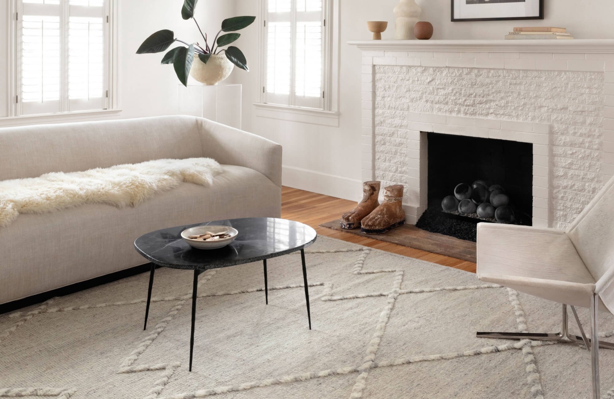Creamy white curved sofa and modern chair on a textured hand knotted ivory rug with raised geometric patterns, set in a bright, airy room.