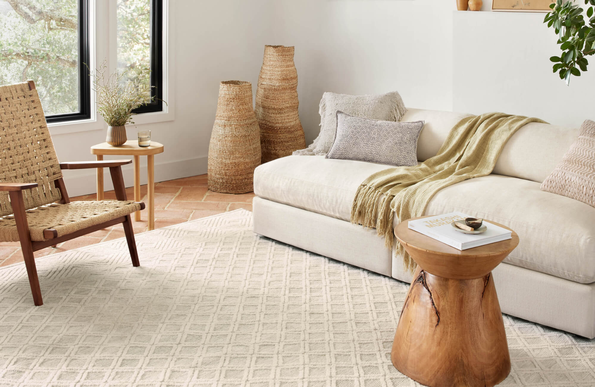 Soft beige sectional sofa and woven accent chair rest on a cream diamond-textured power loomed rug, creating a cozy, sunlit nook.