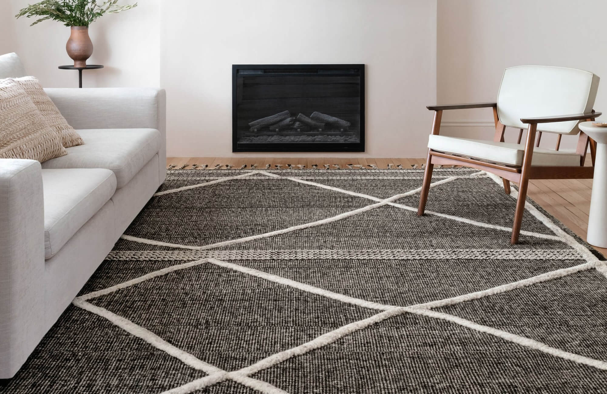Light gray sofa and white-cushioned armchair contrast with a hand knotted charcoal rug with bold ivory crisscross lines in a modern, serene living room.