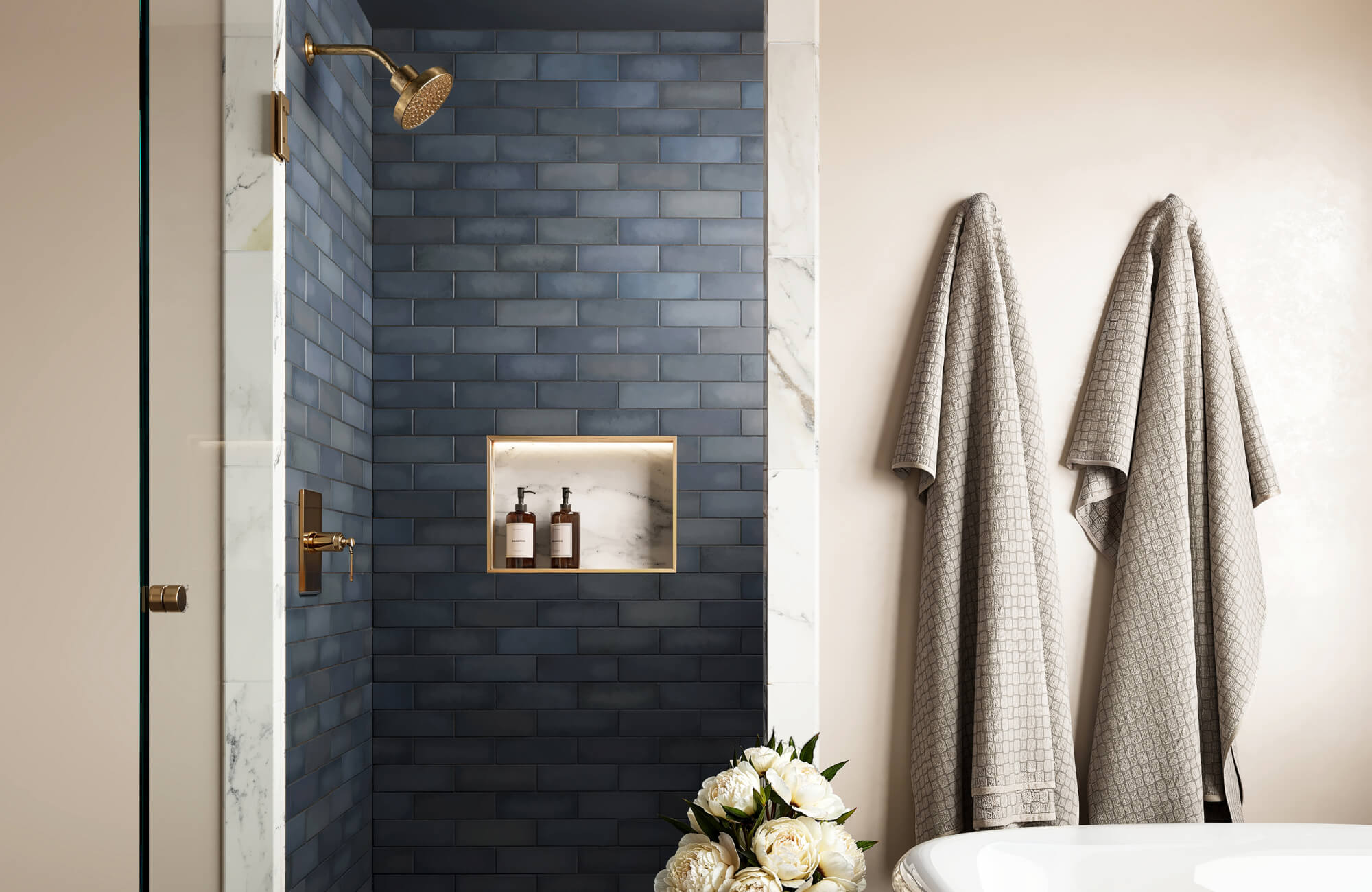 null Shower with horizontal deep blue tiles and brass accents, softened by light walls and textiles, creating a relaxed, spa-like atmosphere while subtly expanding the room’s width.