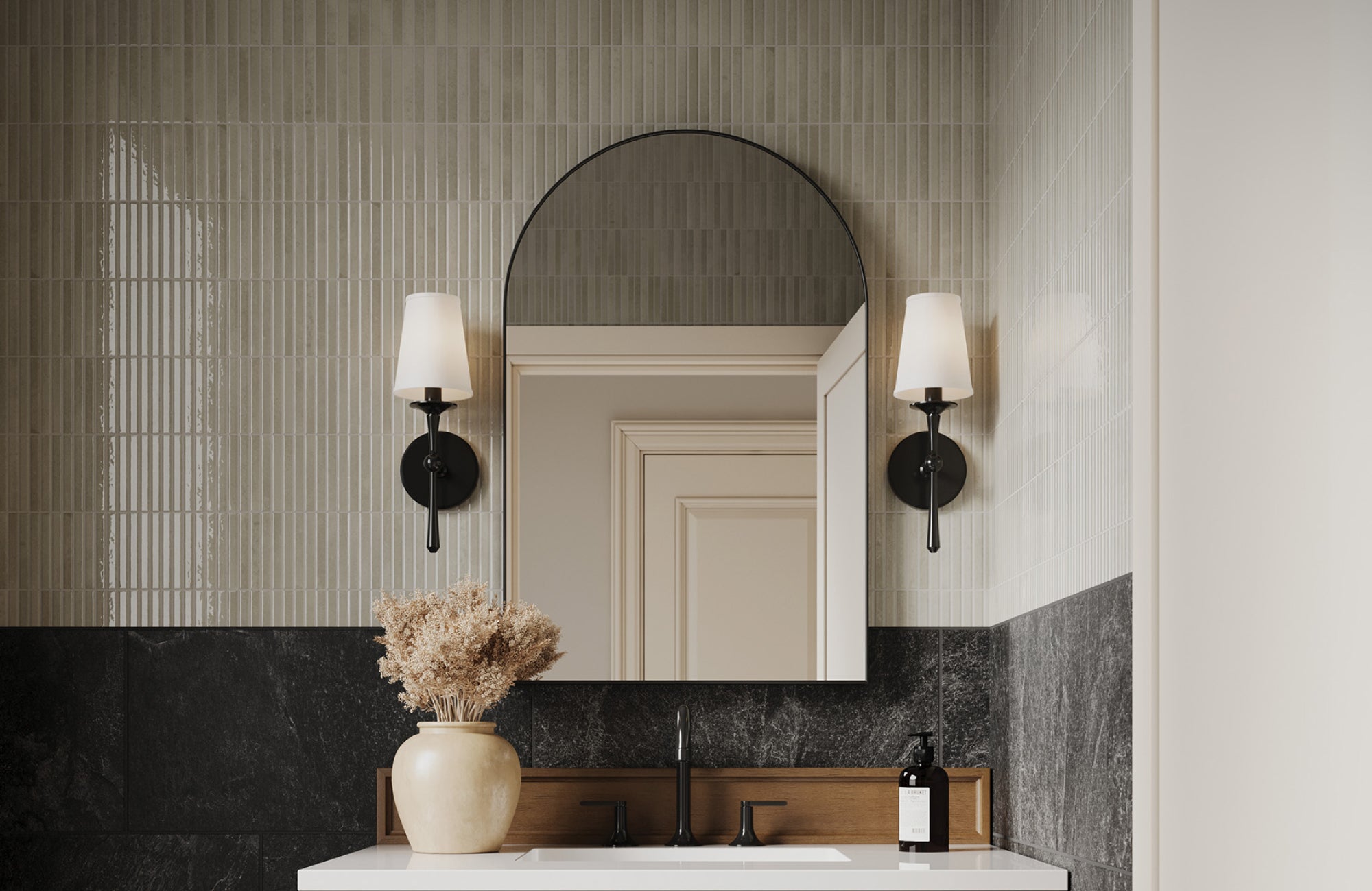 Black sconces with tapered white shades frame a round mirror, enhancing contrast in a minimalist black-and-beige bath.