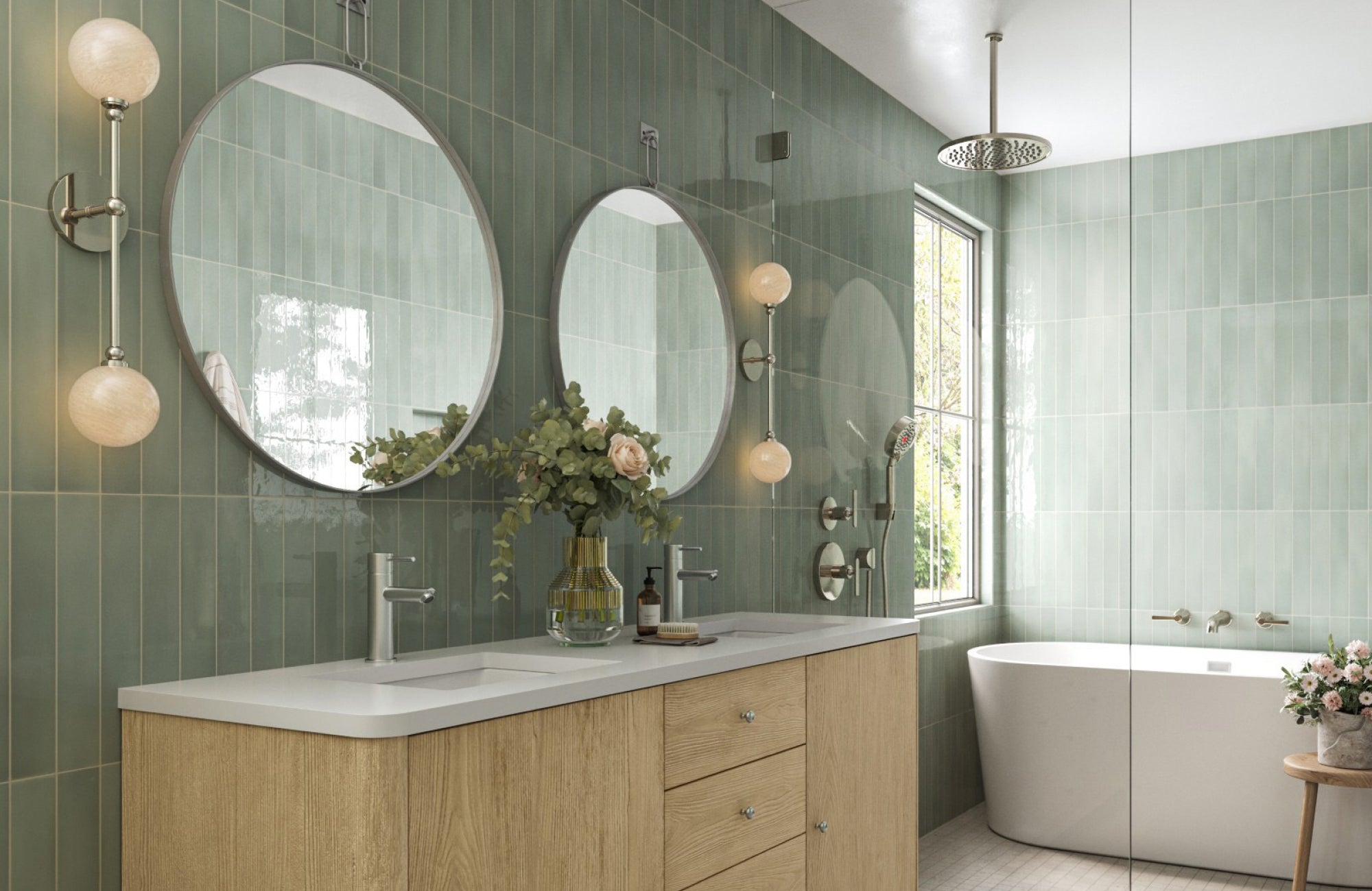 Double-globe sconces in polished nickel frame circular mirrors in a fresh, green-tiled bathroom with natural light.