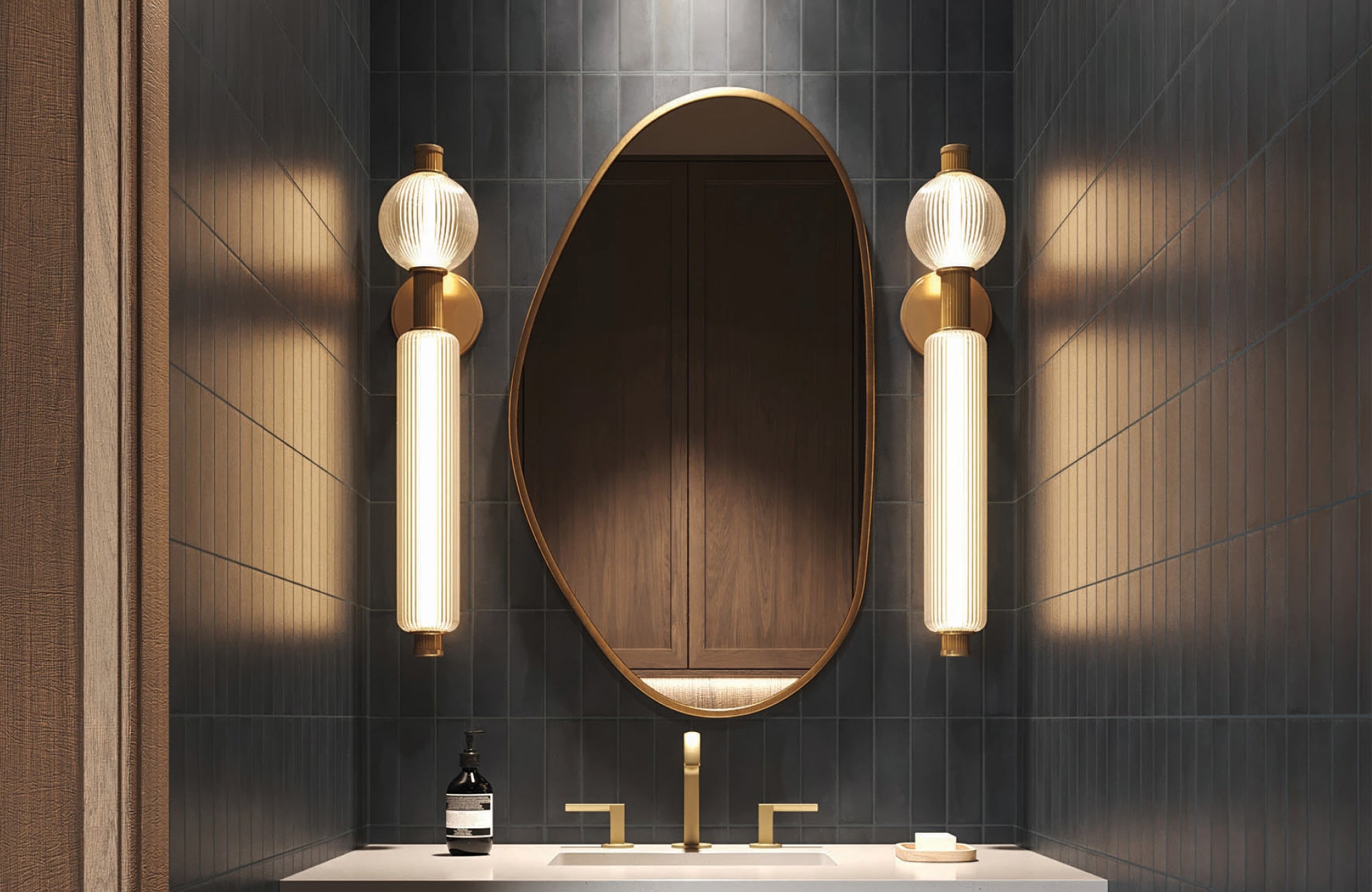 Tall vertical sconces flank an asymmetrical mirror in a dark-tiled powder room, delivering soft, layered lighting.