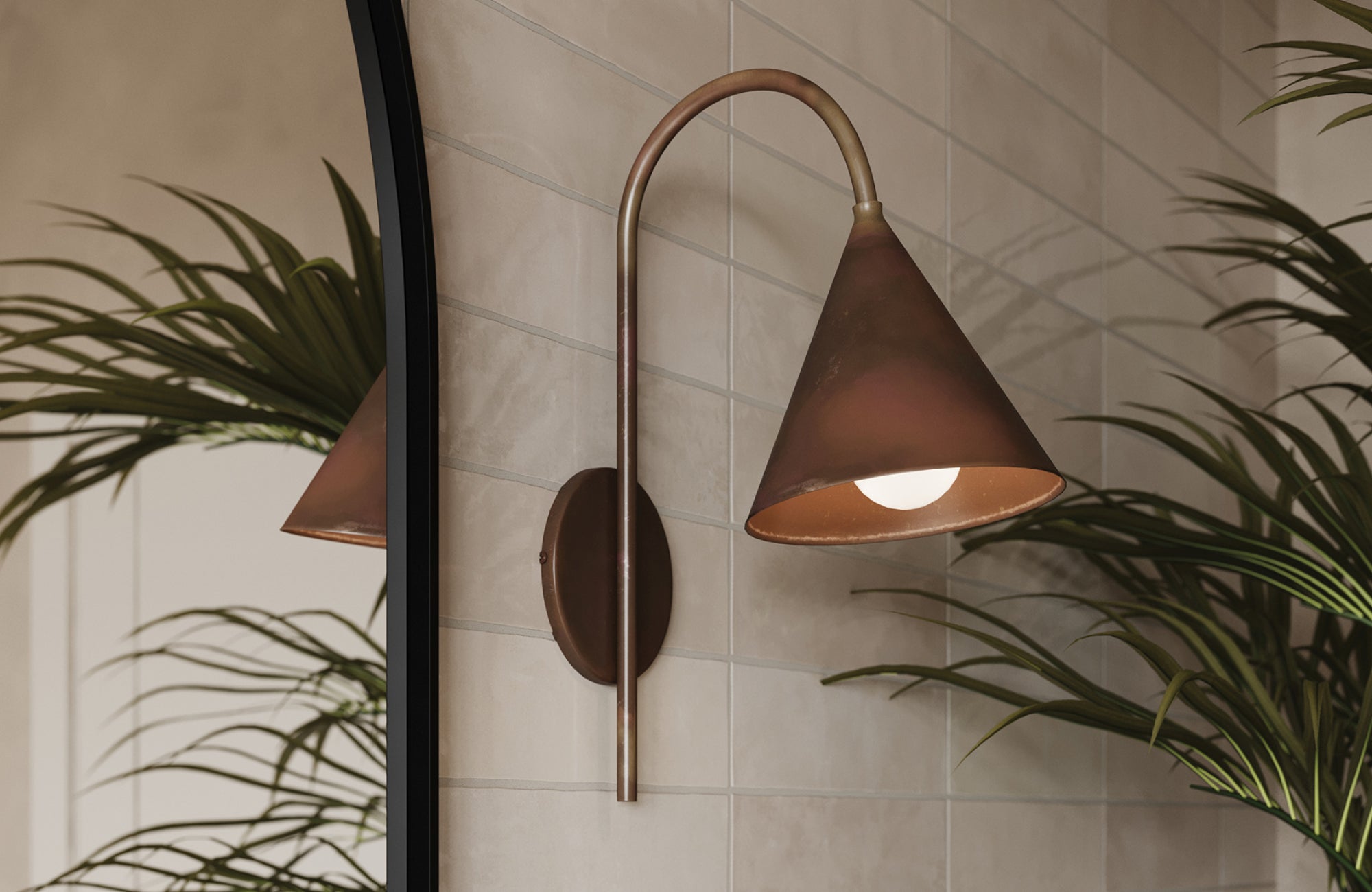 Curved bronze wall sconce with cone shade casts light downward, highlighting natural textures in a tiled hallway.