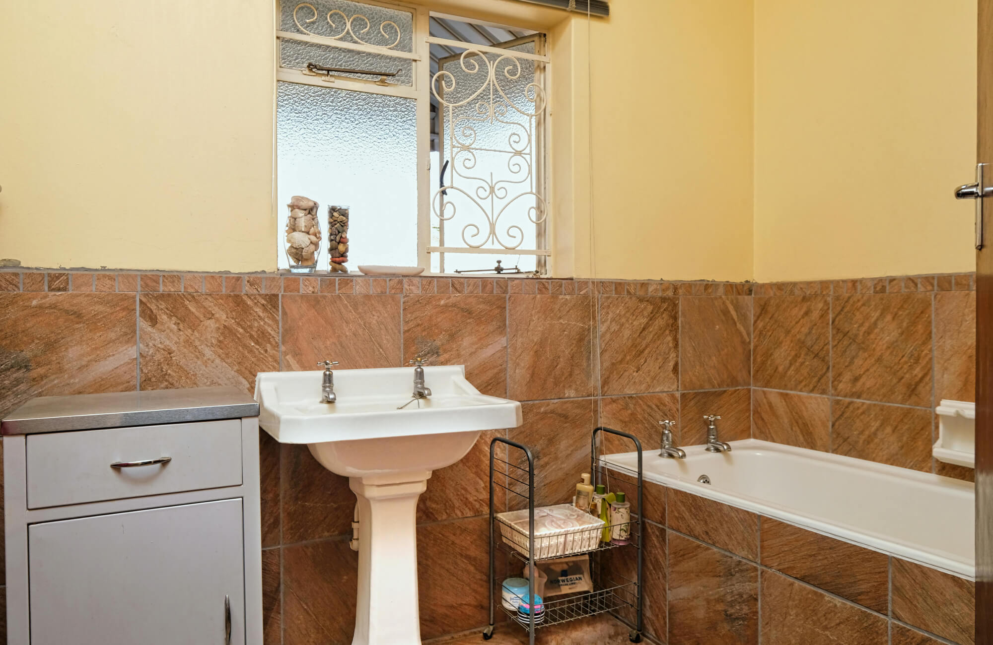 null Pedestal sink centered in a narrow bathroom with warm tile walls and minimal cabinetry, illustrating how this sink style prioritizes visual openness over built-in storage.