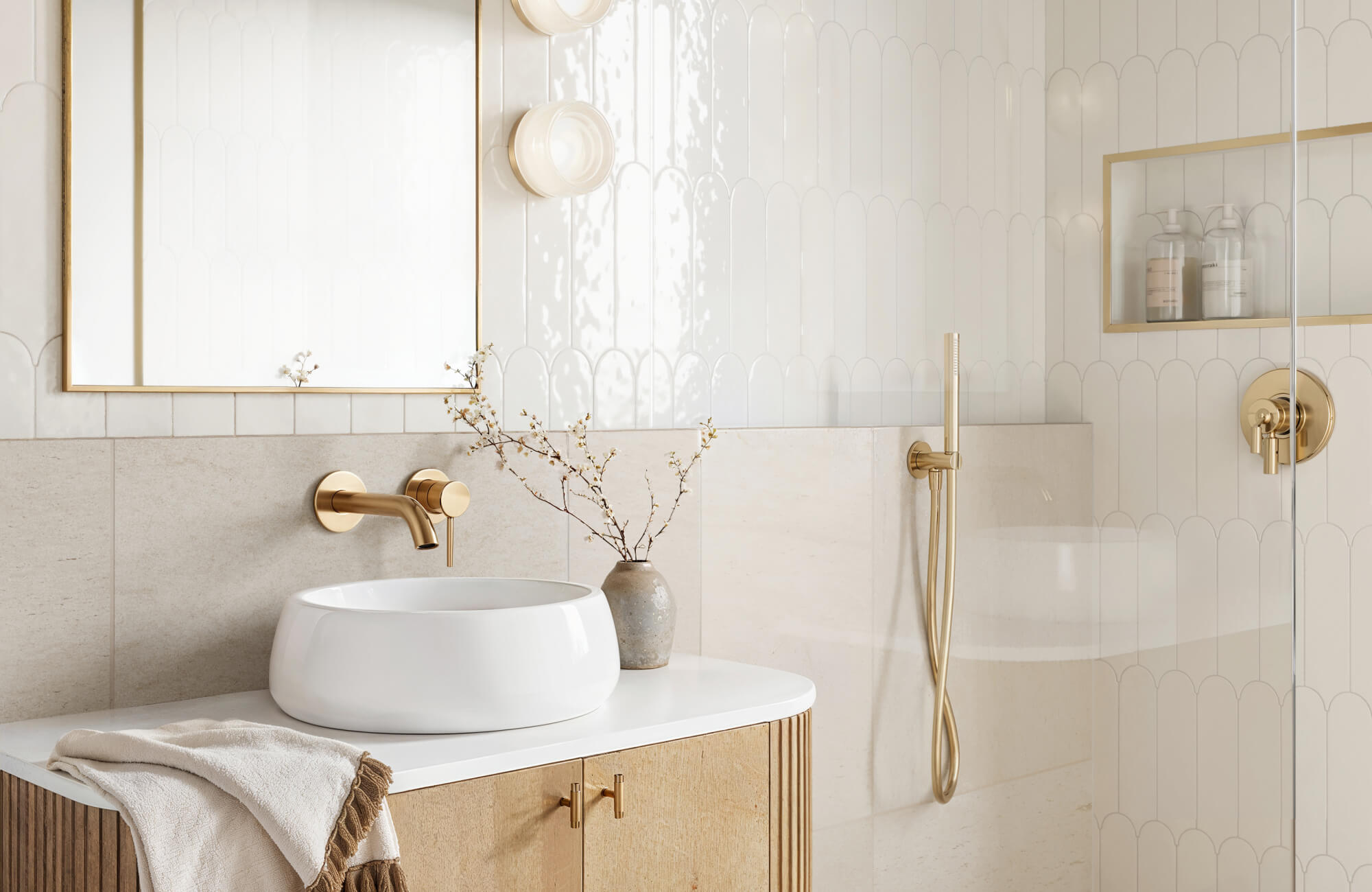 null Bright bathroom vanity and shower area with half-height neutral wall tile, glossy white upper shower tile, brass fixtures, and a glass enclosure.