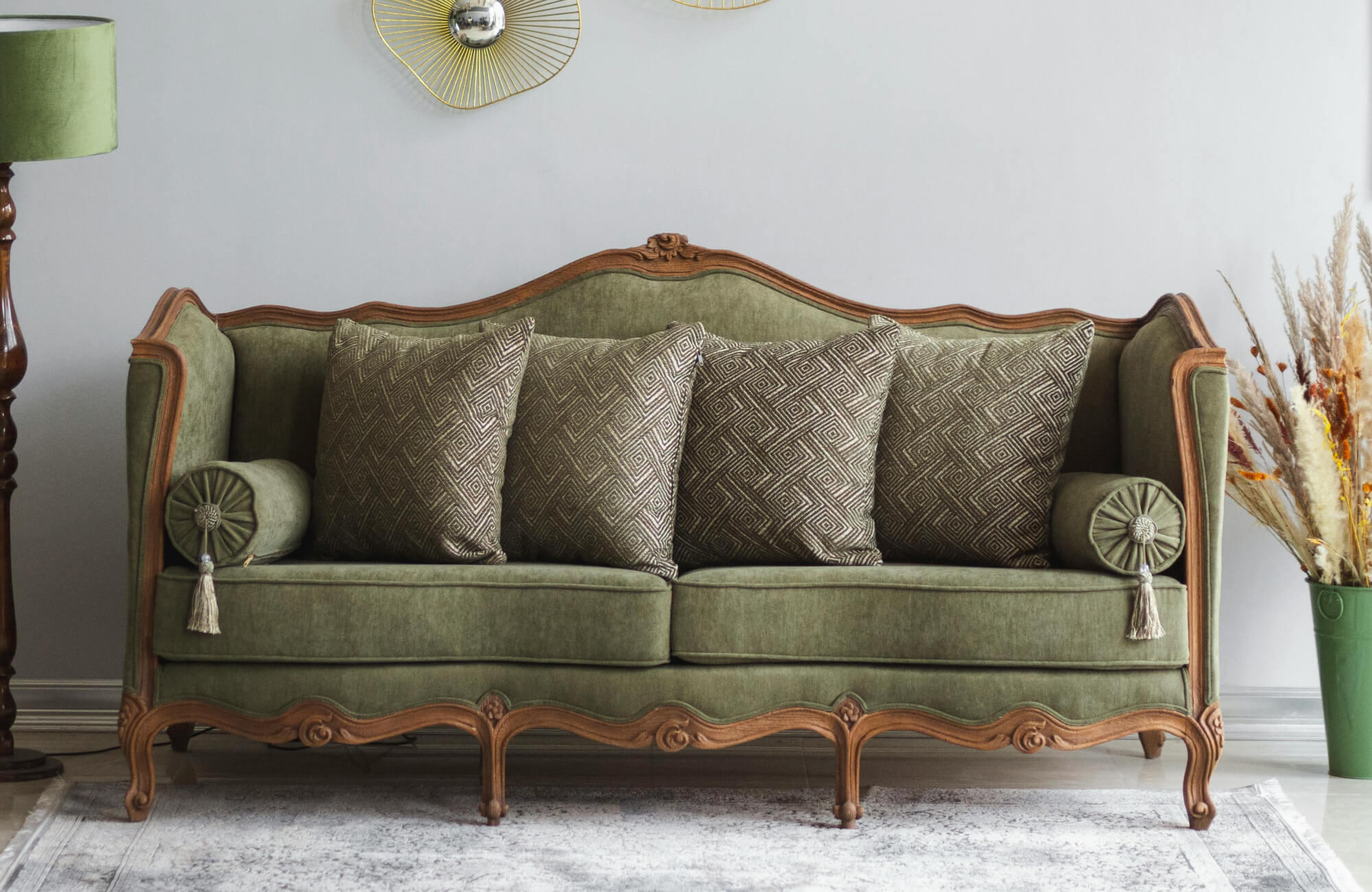null Vintage olive green velvet sofa with carved wood trim, styled with geometric throw pillows and bolster cushions.
