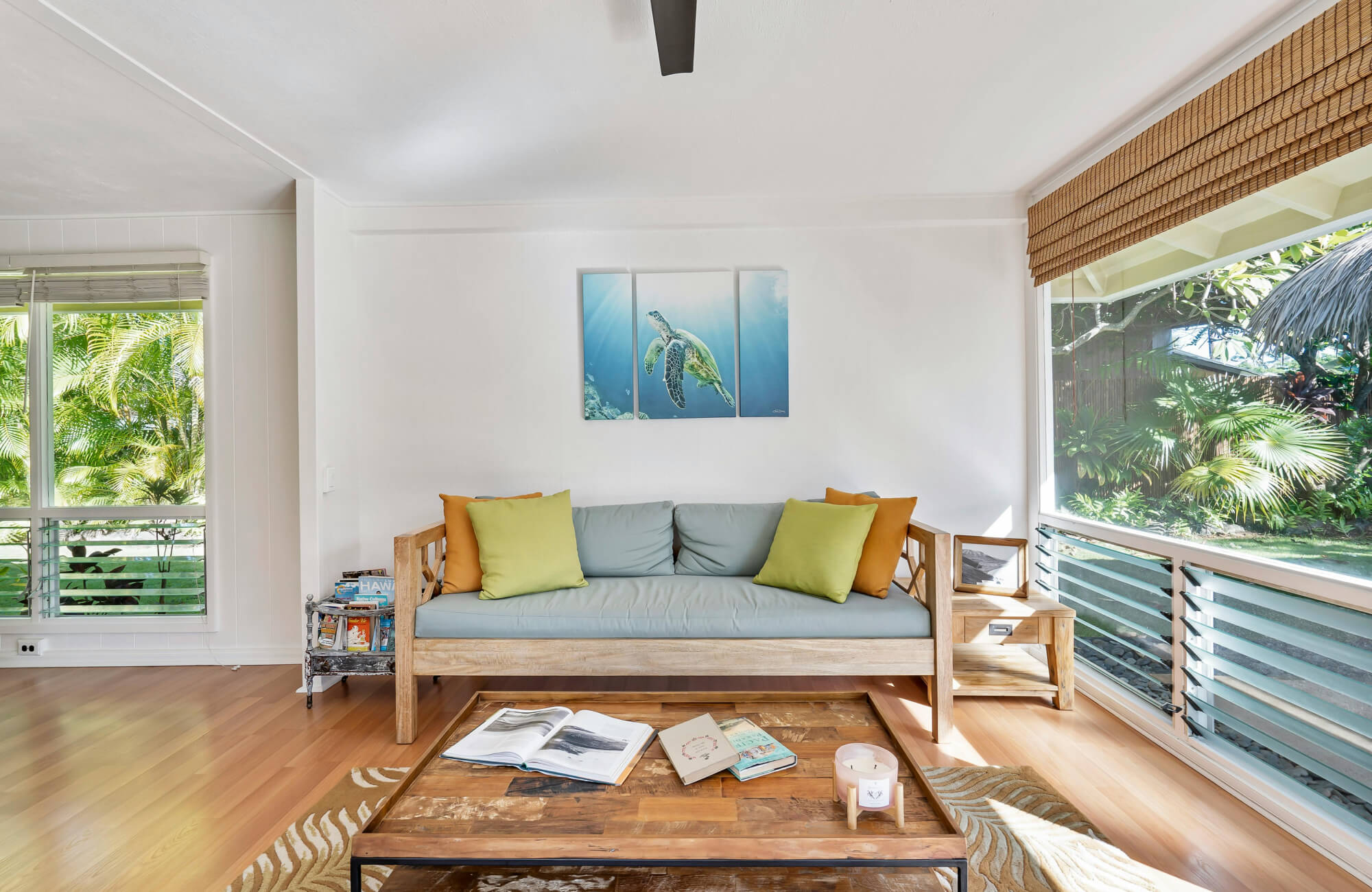 null Airy living room with warm wood flooring, light wood sofa with green accent pillows, and tropical garden views.