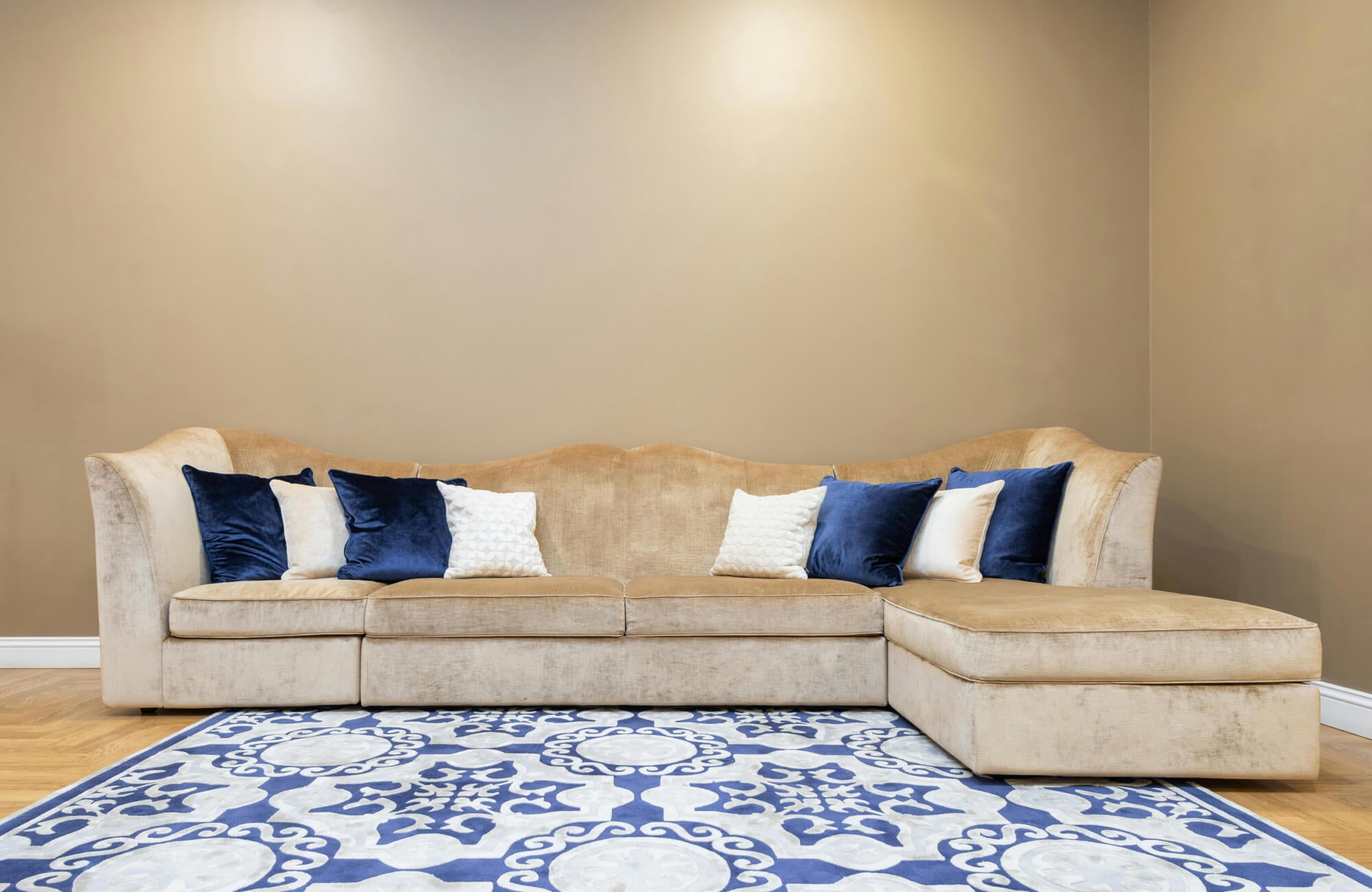 null Contemporary beige sectional sofa with navy and ivory velvet decorative pillows, set on a bold blue patterned tile rug.