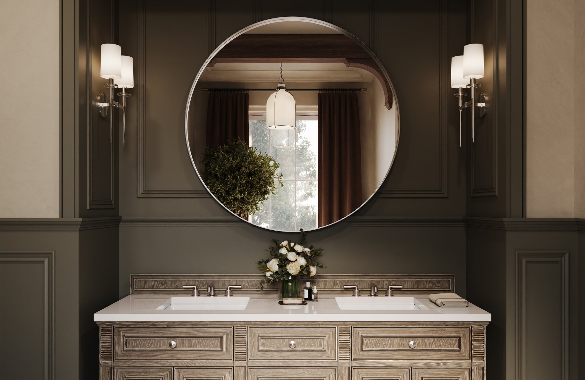 A spacious double-sink vanity with a round mounted mirror and soft white sconces, surrounded by rich paneled walls and warm accents reflected from the window beyond.