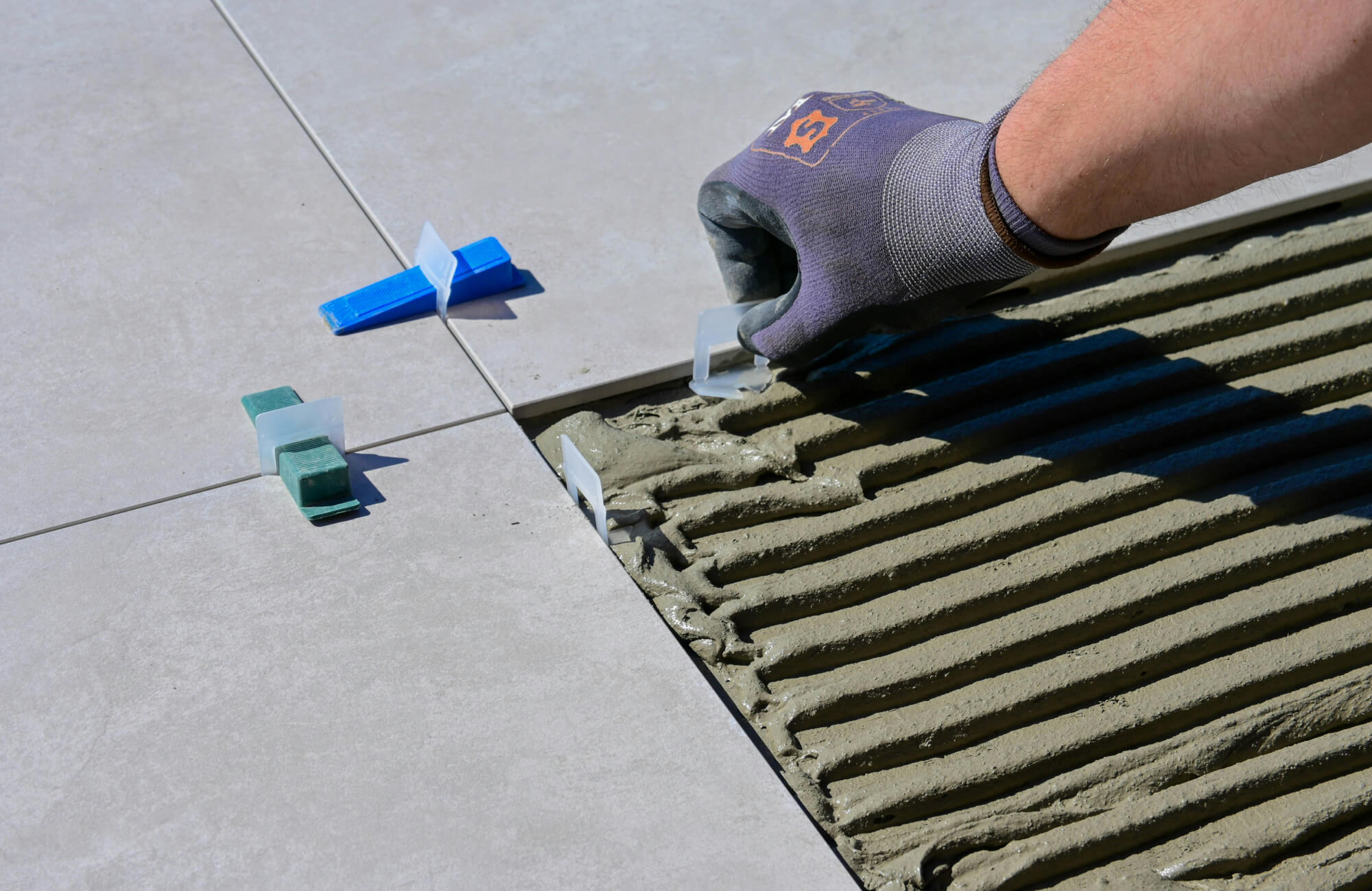 null Close-up of a tile installation process, showing large format porcelain bathroom tiles being laid with adhesive and leveling spacers for a precise finish.