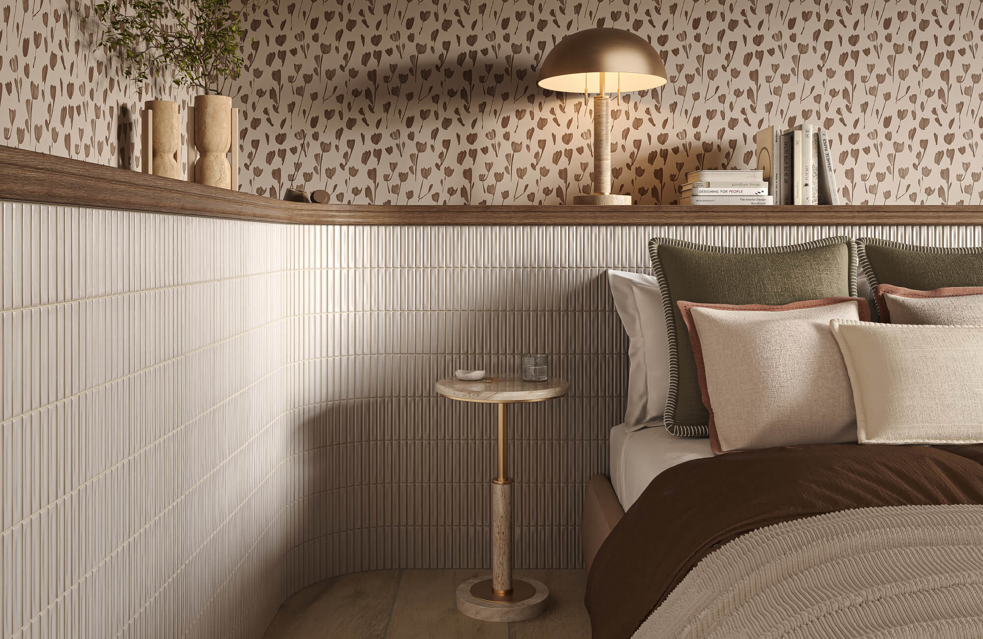 Bedroom corner with layered throw pillows in green, blush, cream, and white arranged against a bed with a dark brown blanket, beside a small round table and lamp.