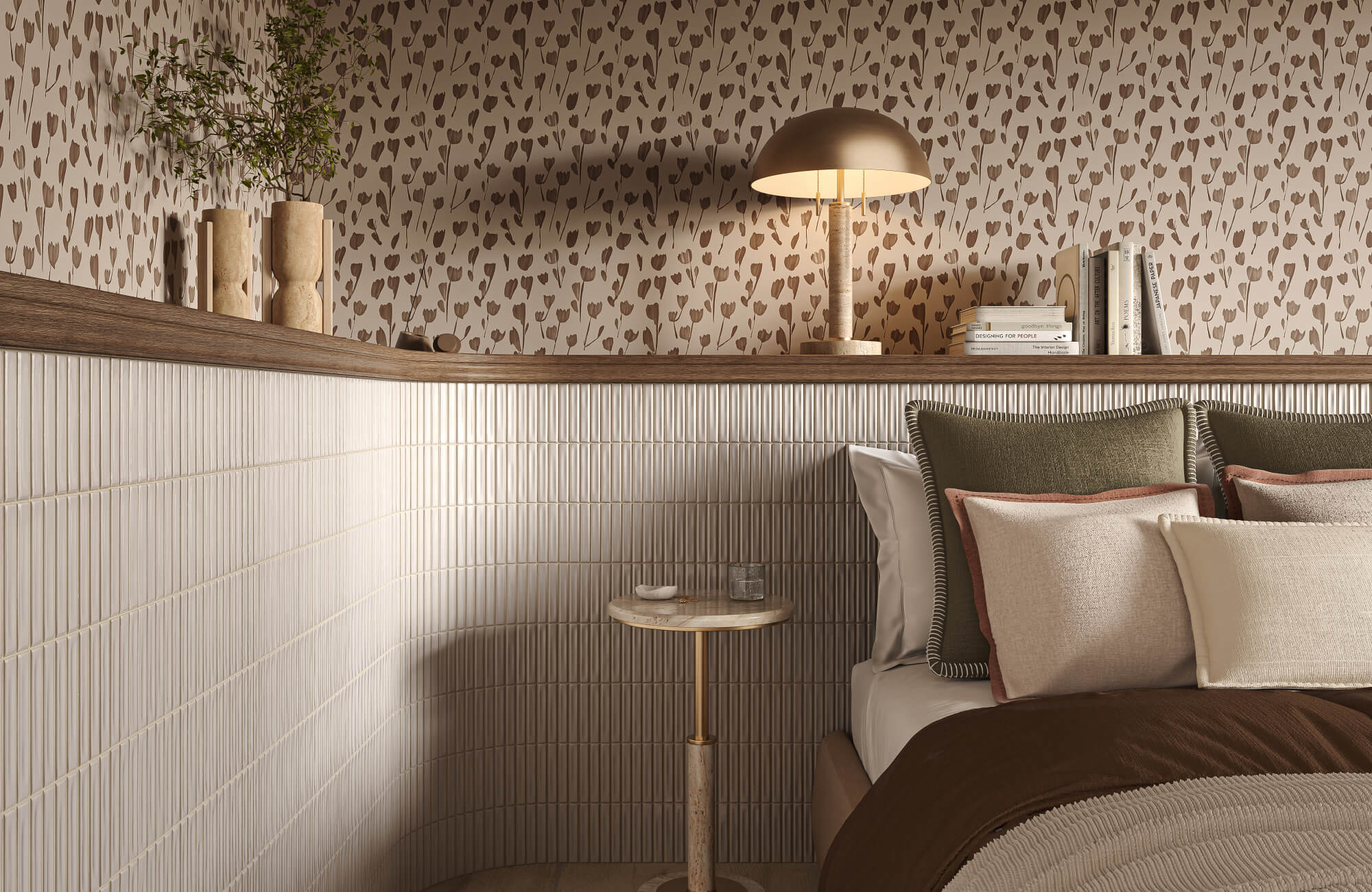 Bedroom corner with layered pillows, brown floral wallpaper, slim cream wall tile, a wood ledge, and a small round bedside table with a lamp.