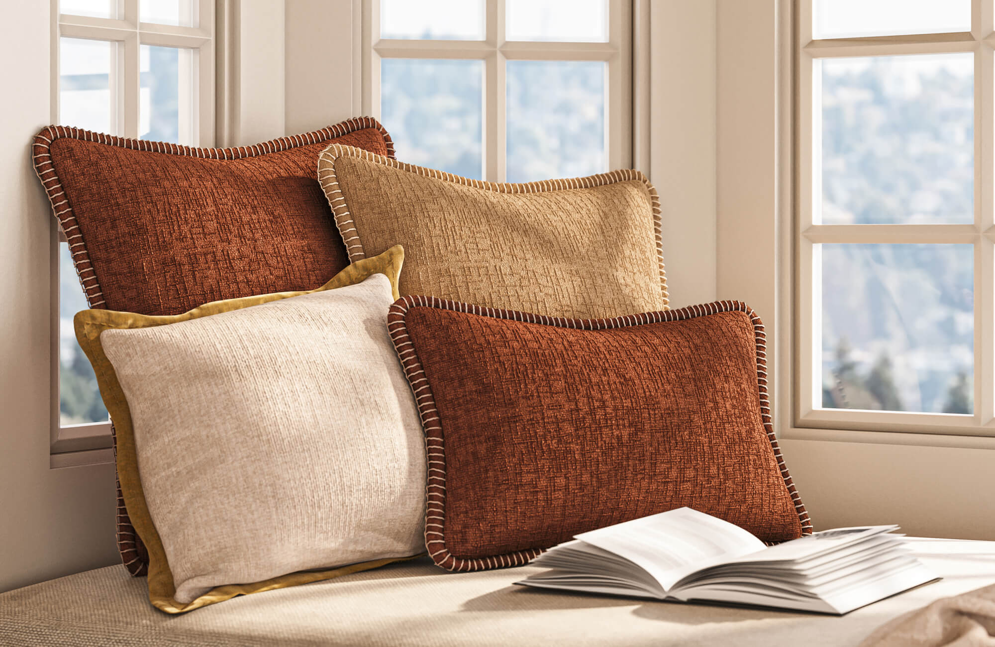 Stacked decorative pillows in cream, mustard, terracotta, and tan sit beside tall windows with an open book in the foreground.