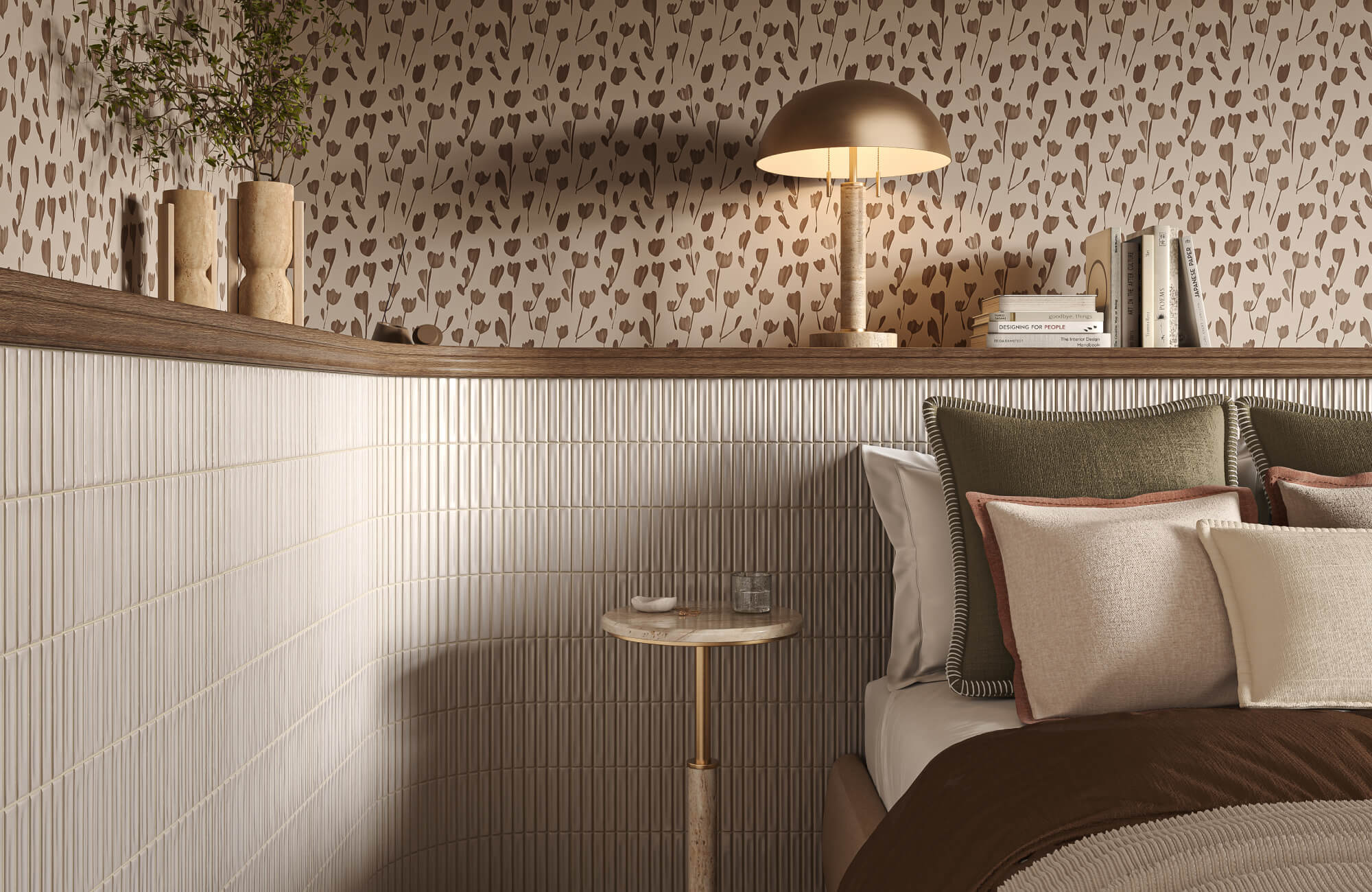 Layered throw pillows on a bed beside ribbed wall tile, floral wallpaper, and a brass table lamp.