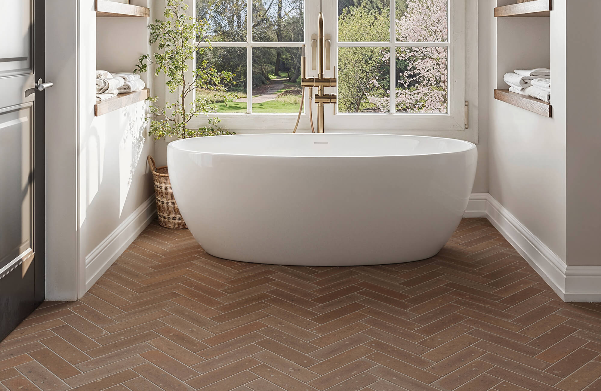 null Serene bathroom featuring a freestanding white tub framed by windows and warm brown herringbone tile flooring, blending natural light and earthy tones for a calming, spa-like retreat.