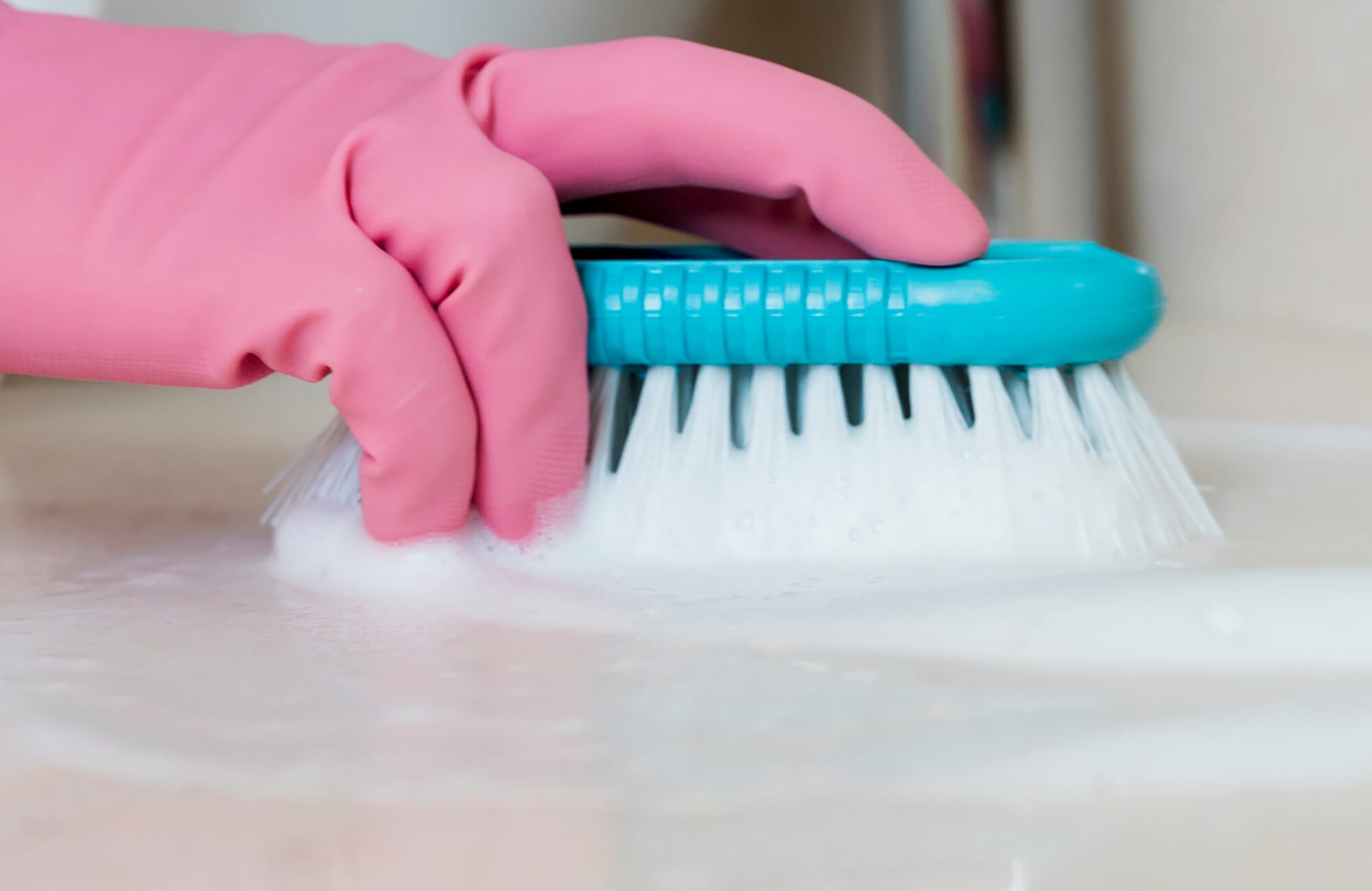 null Close-up of a hand wearing pink rubber gloves scrubbing a soapy surface with a blue cleaning brush, emphasizing cleanliness and maintenance in home care.