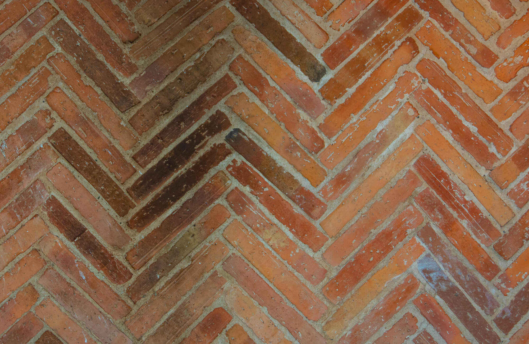 null Rustic red brick surface arranged in a herringbone pattern, showcasing a blend of warm earthy tones and textured mortar joints that add depth and traditional charm.