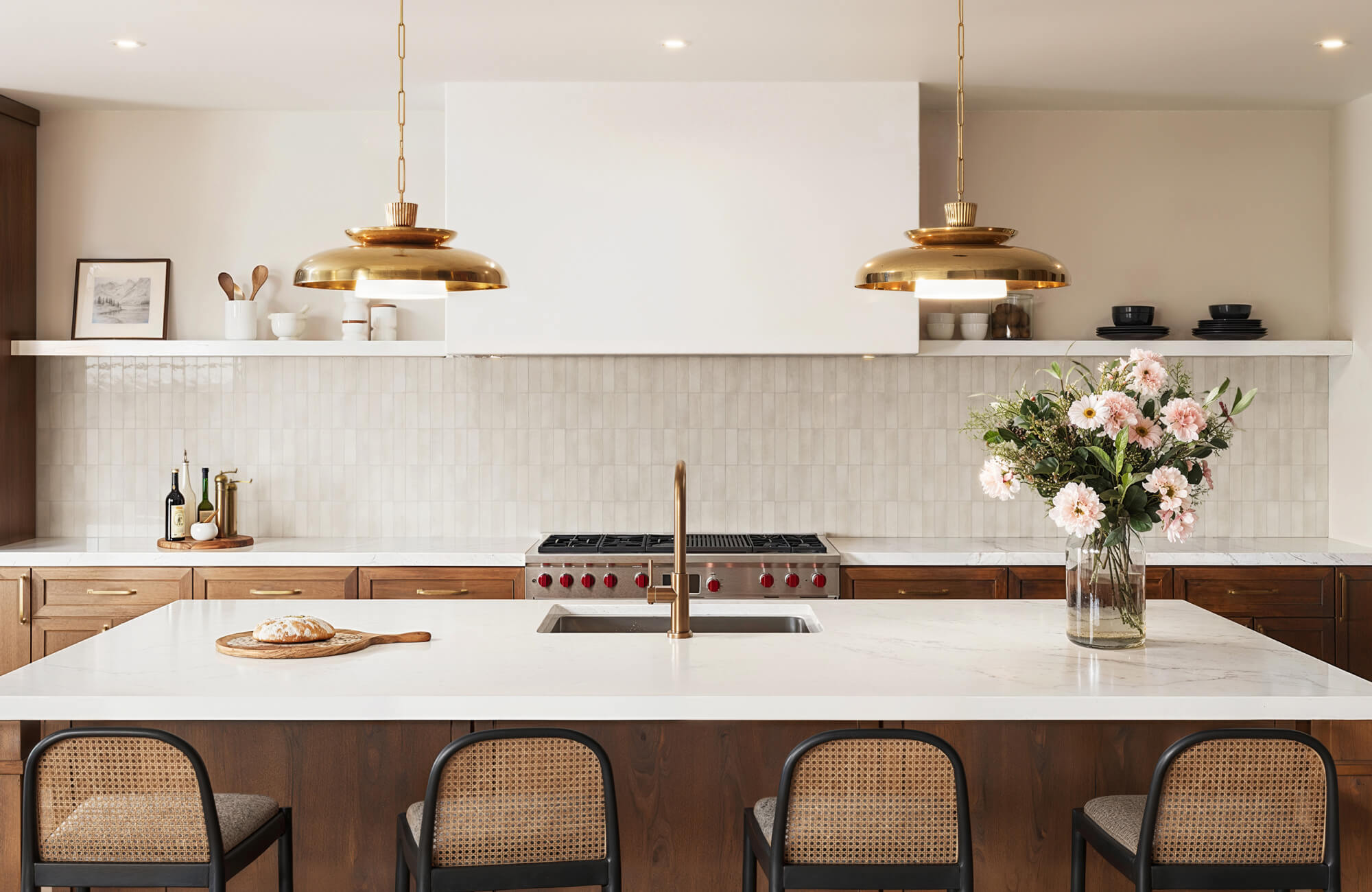 Warm kitchen with vertical glossy subway tiles, brass pendant lights, and a white island topped with fresh florals