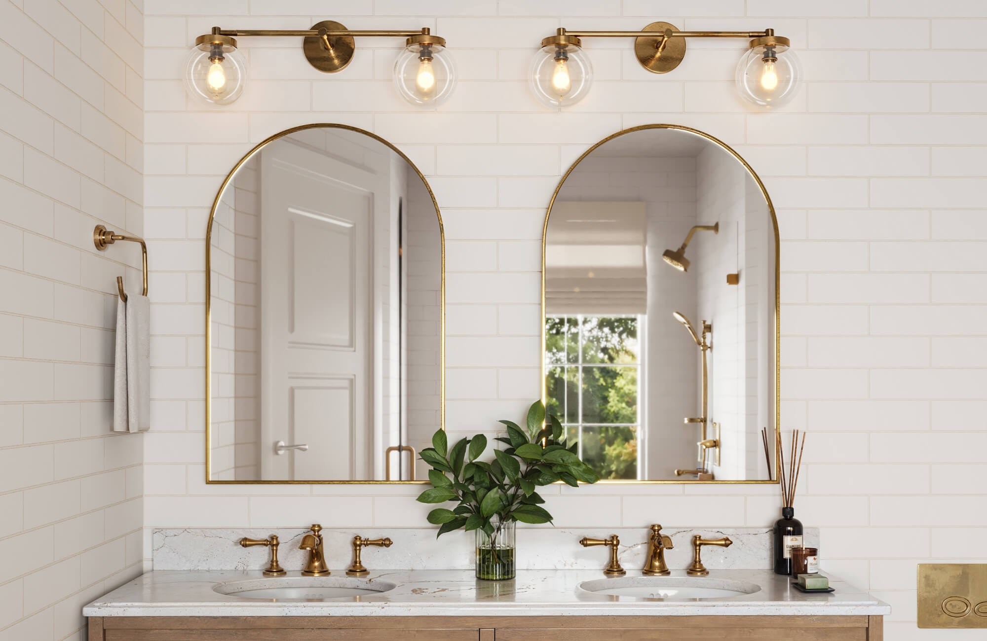 Elegant bathroom with white subway tiles, a double vanity with gold faucets, and two arched mirrors beneath stylish gold light fixtures