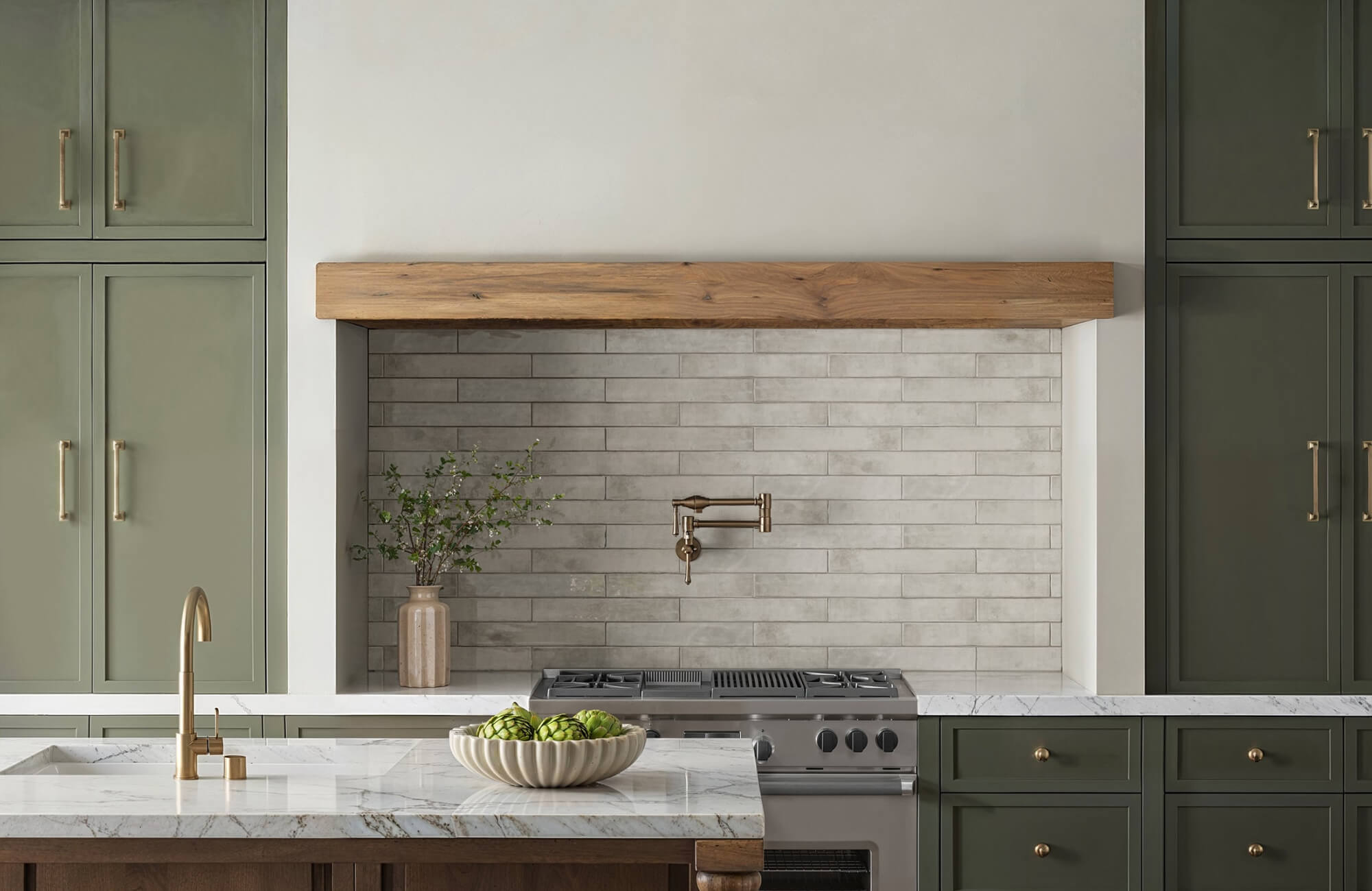 Green shaker cabinets paired with wood accents, marble countertops, and a neutral tiled backsplash for a classic look.