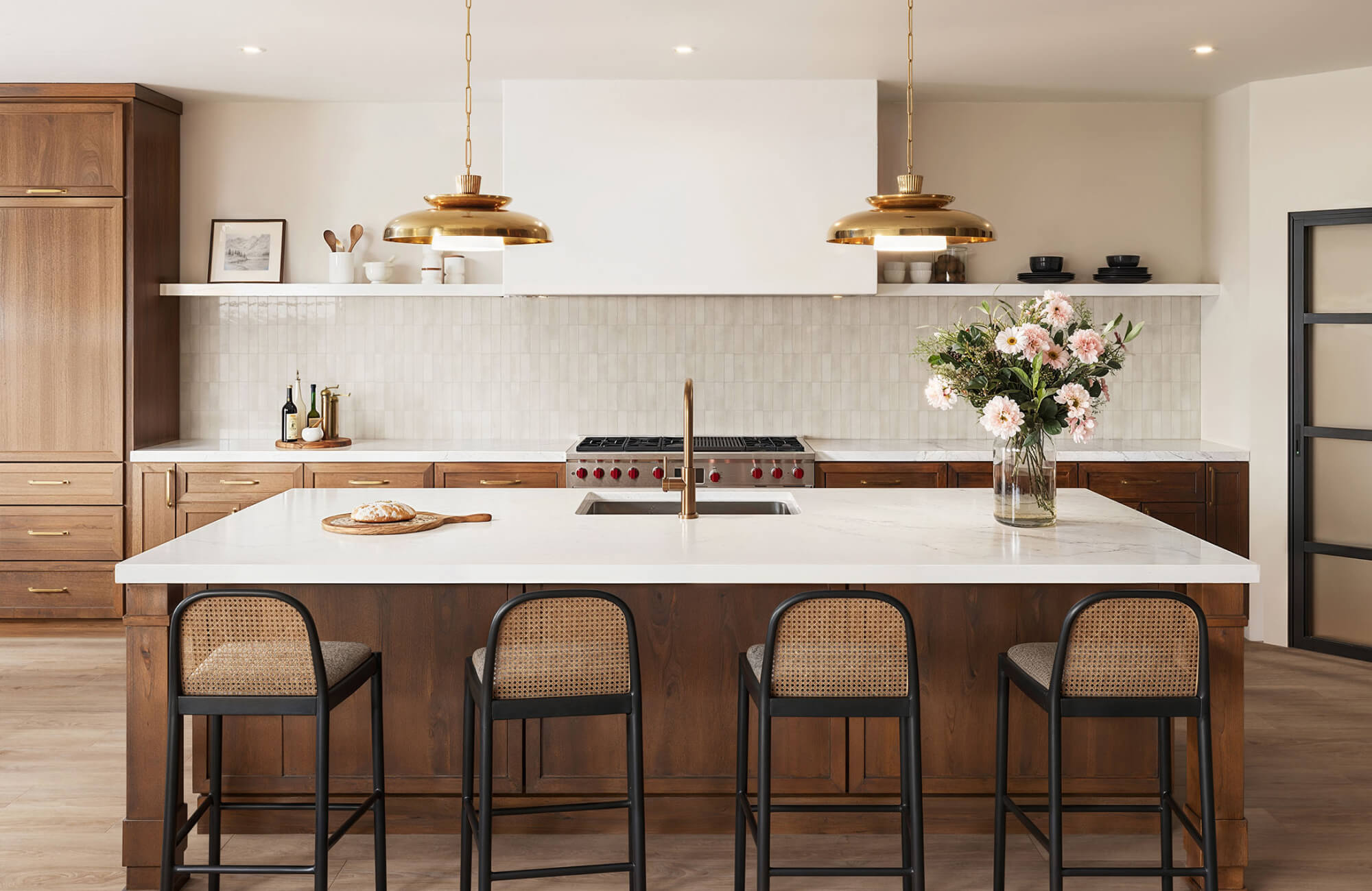 Spacious kitchen island with white countertops, brass pendant lights, and warm wood cabinetry in a timeless layout.