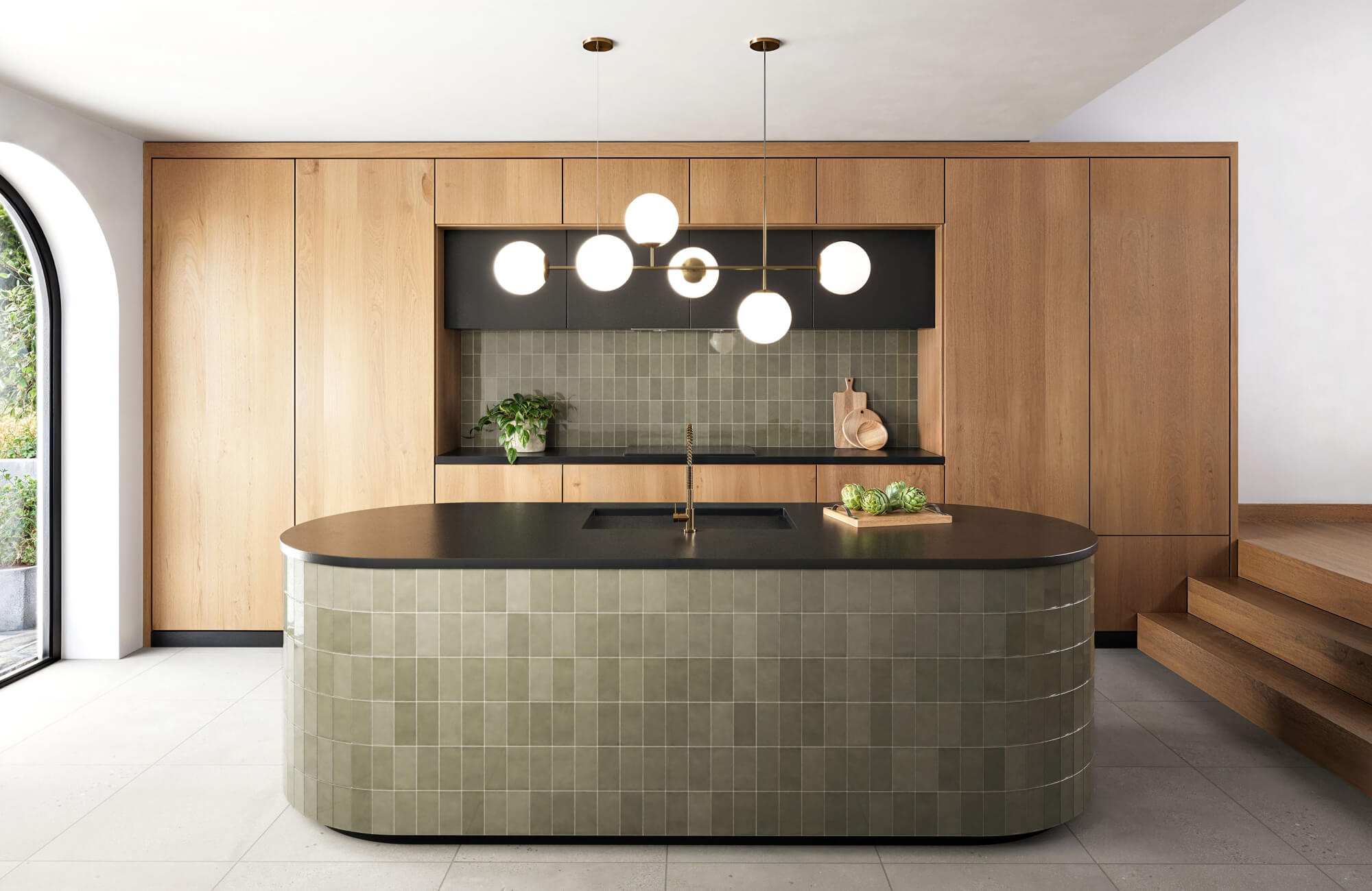 Modern timeless kitchen with curved island, muted green tile, wood cabinetry, and soft globe pendant lights.