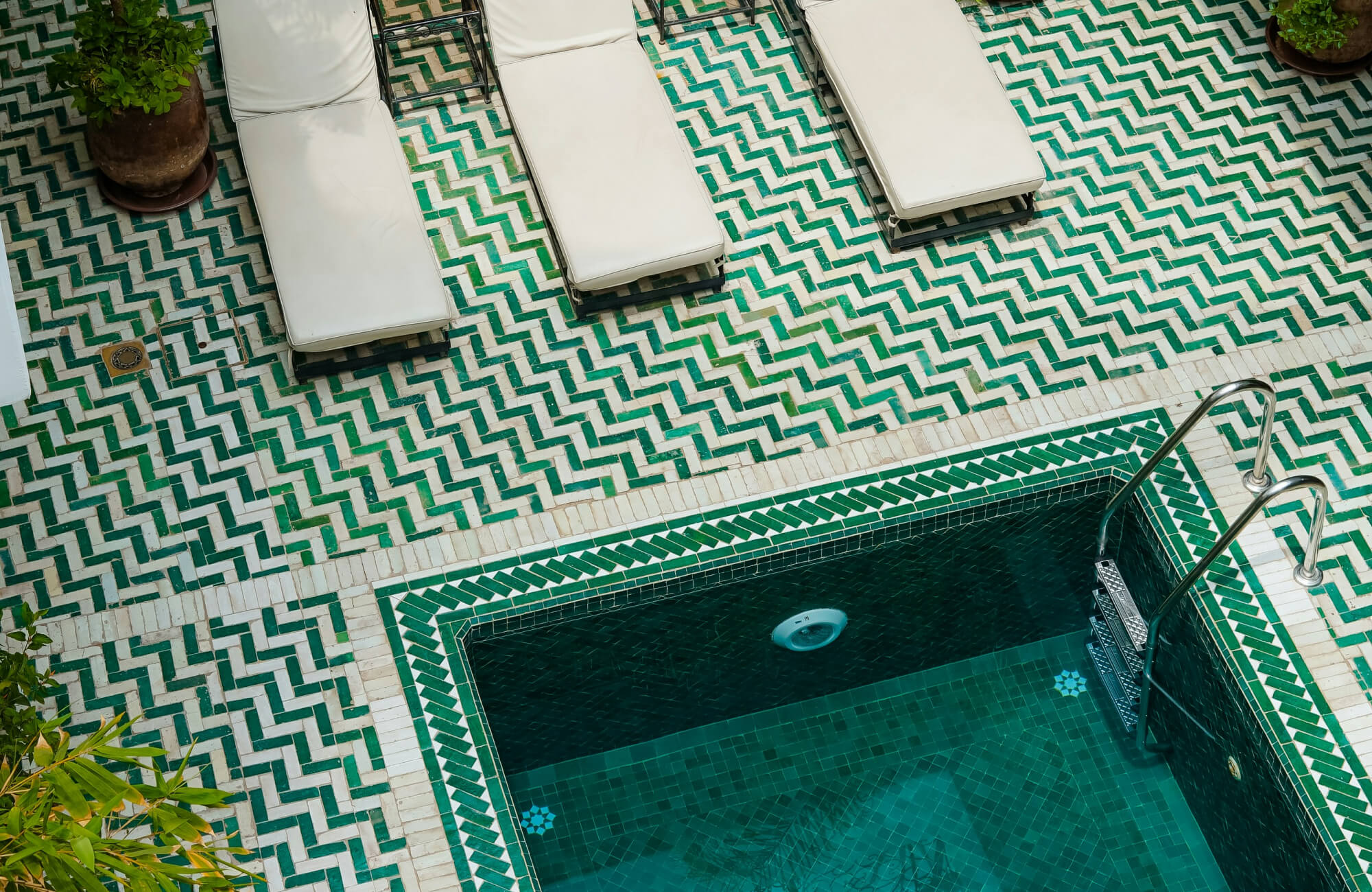 Vibrant green and white herringbone tiles surround a deep emerald mosaic pool, creating a bold, tropical retreat.