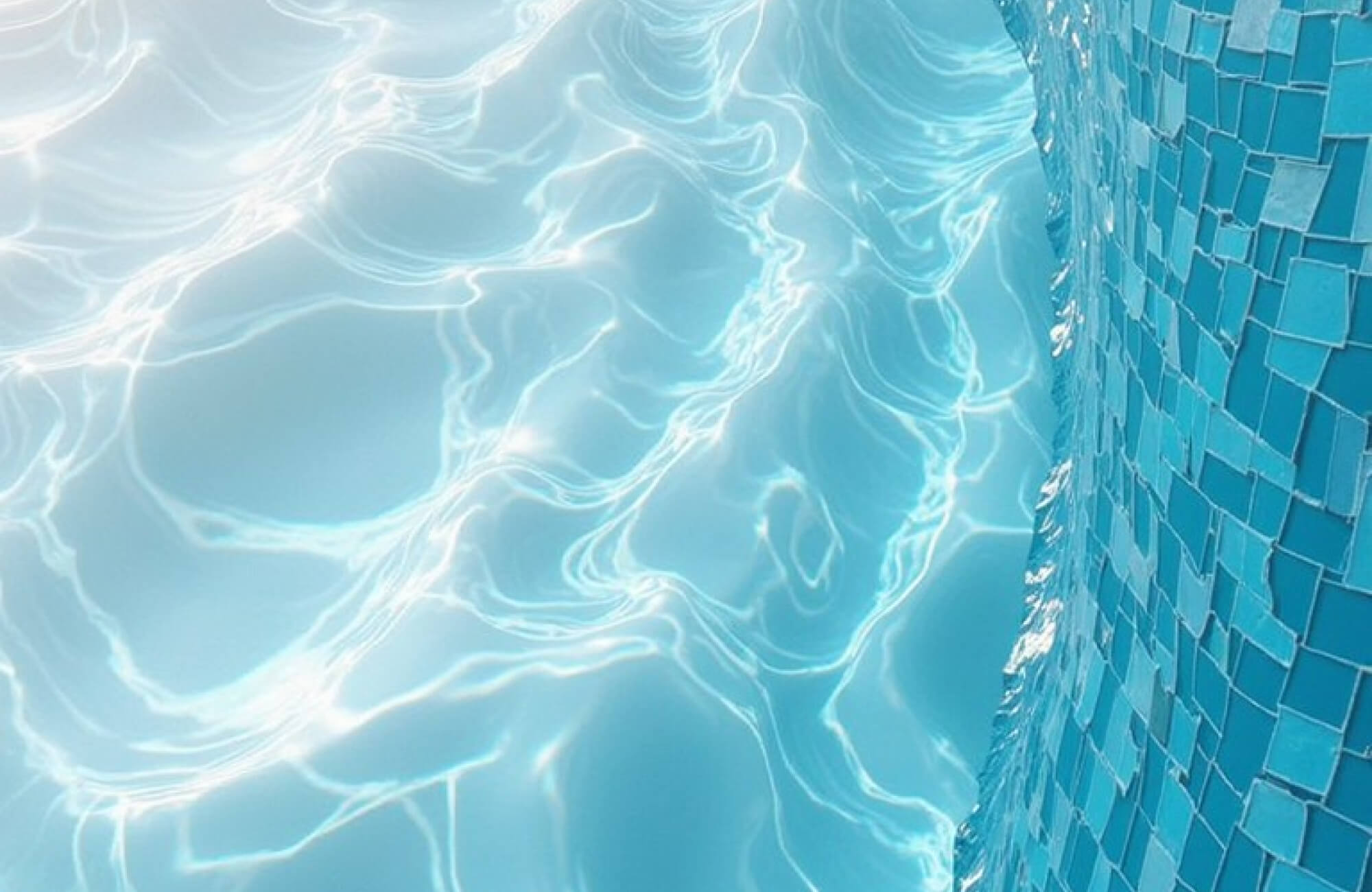 Sunlit pool water ripples beside a curved wall of glossy blue mosaic tiles, creating a serene aquatic shimmer.