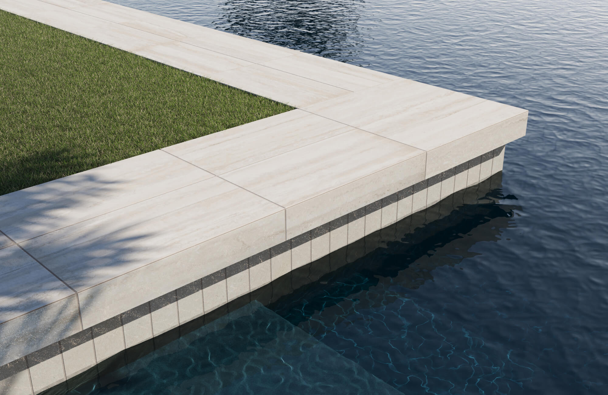 Minimalist poolside with light travertine-style coping tiles and deep blue water, bordered by manicured green grass.