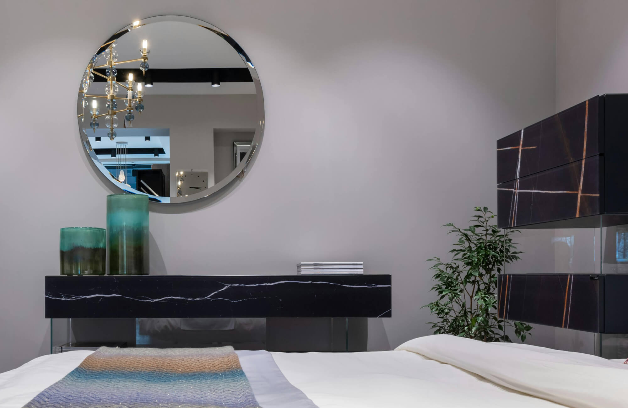 null Contemporary bedroom with round wall mirror, black marble console, teal glass vases, and soft neutral bedding.