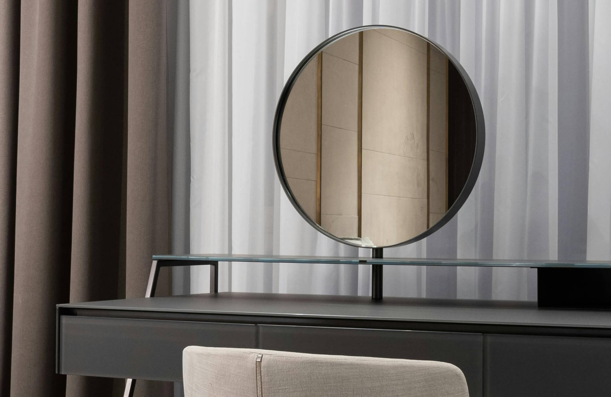 null Modern vanity setup with a round tabletop mirror, glass shelf, dark desk, and layered neutral curtains in the background.