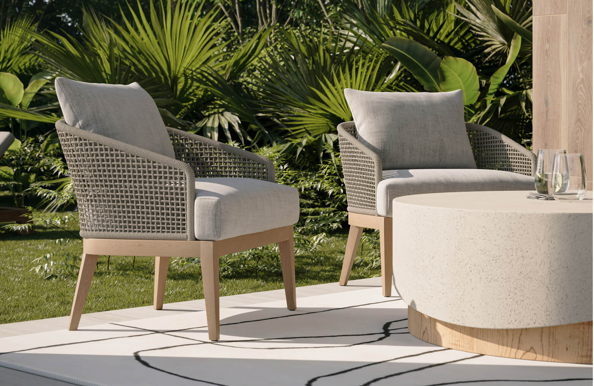 Lush garden patio with teak outdoor furniture, showcasing two cushioned armchairs and a round table.