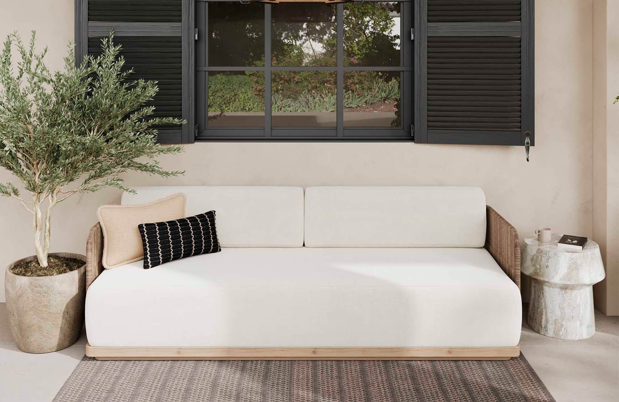 Relaxed patio scene with teak outdoor furniture, featuring a cushioned daybed, accent pillows, and a side table.
