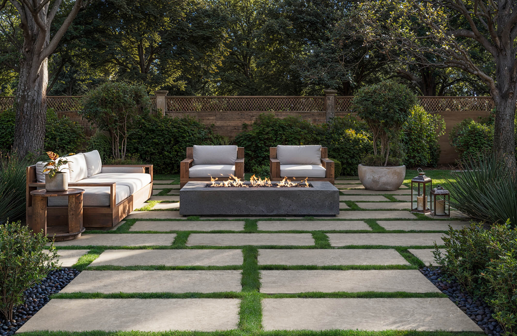 null Inviting outdoor lounge featuring large beige paver tiles set in grass joints, complemented by wooden seating, a sleek fire pit, and lush greenery that together create a warm, modern retreat.