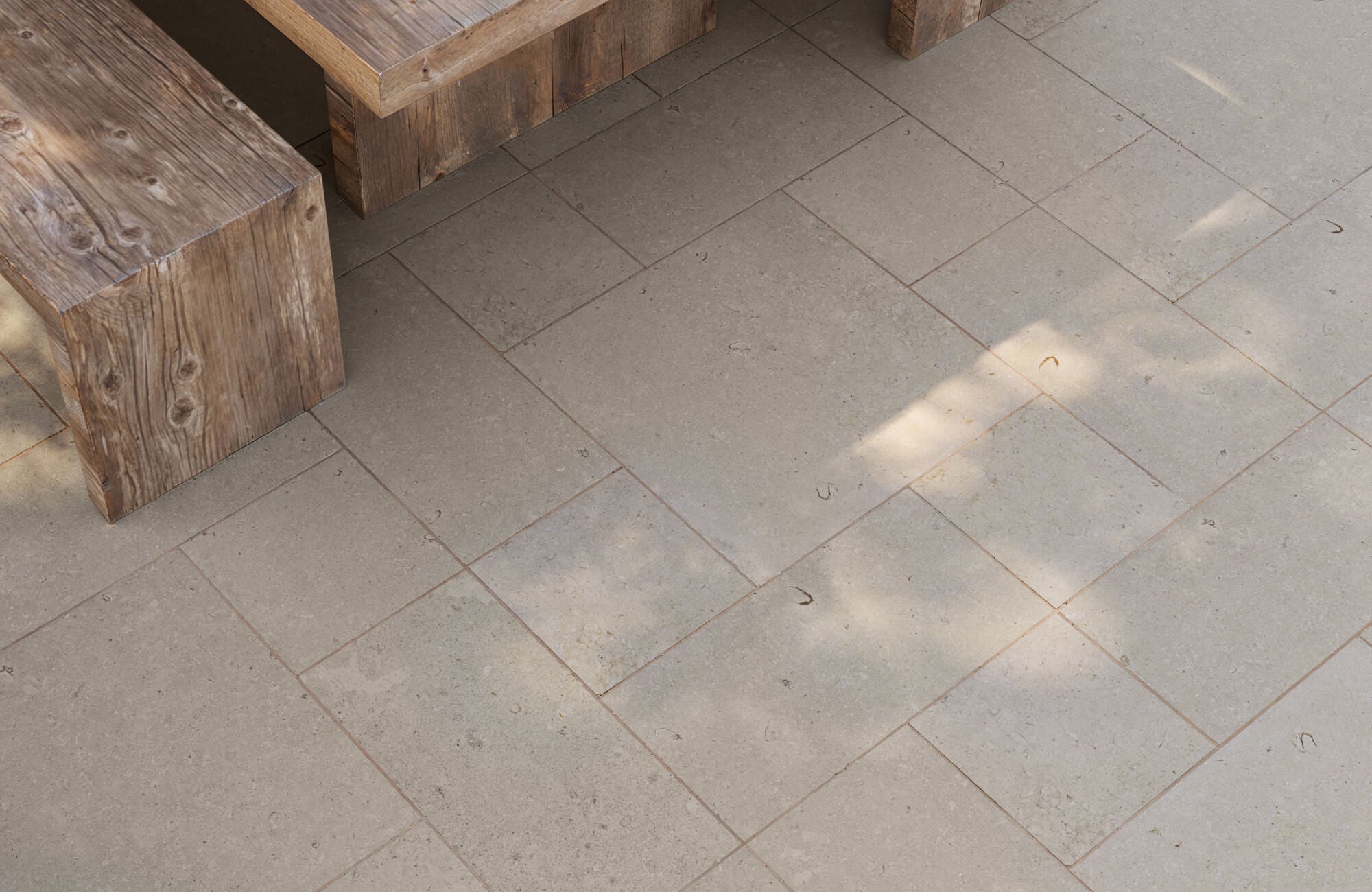null Outdoor seating area featuring taupe stone-look paver tiles in a modular pattern, paired with rustic wooden benches that highlight the natural texture and warmth of the space.