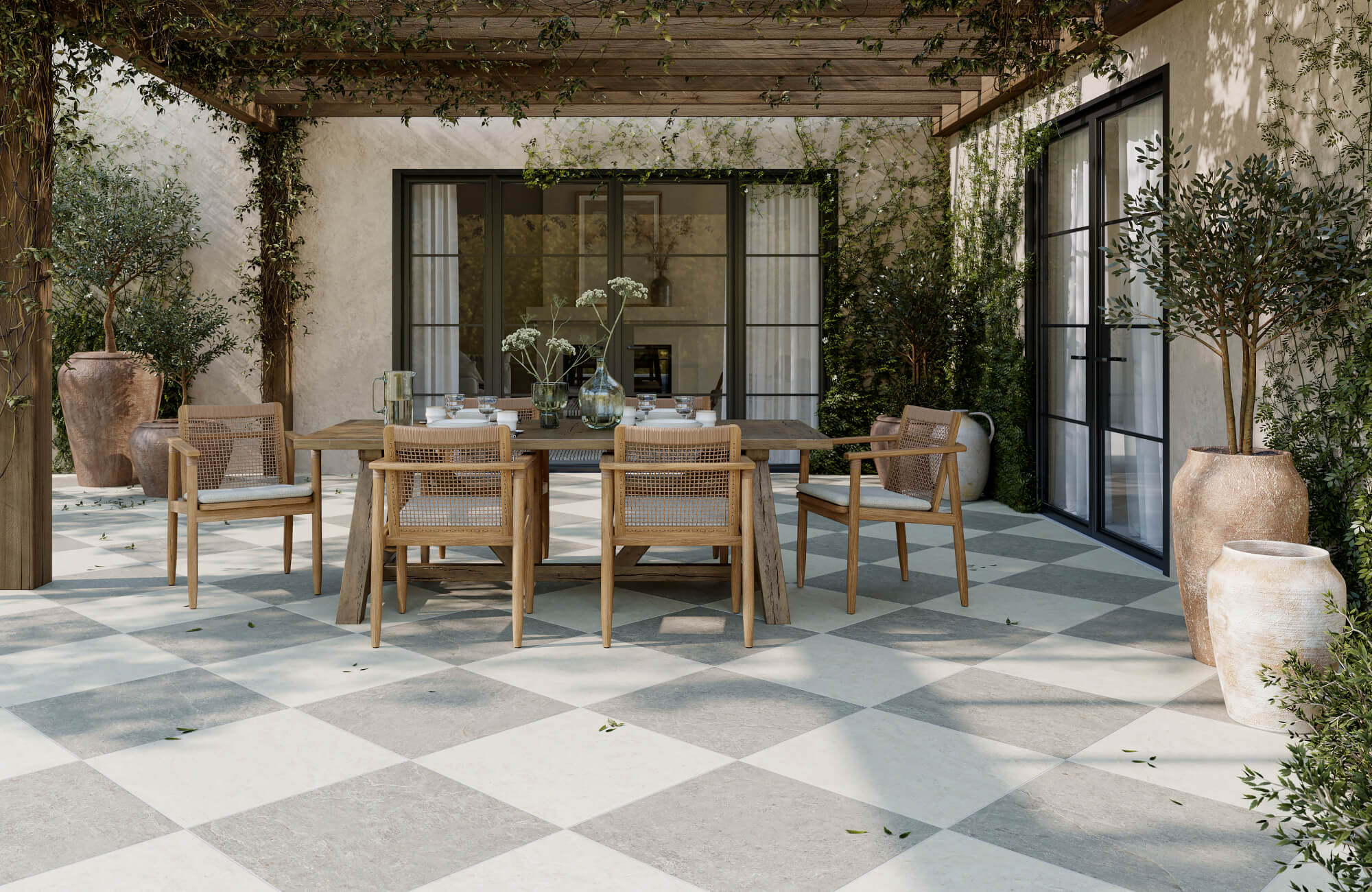 null Charming outdoor dining space featuring large checkered paver tiles in soft gray and cream tones, paired with natural wood furniture and lush greenery under a vine-covered pergola for a relaxed, Mediterranean-inspired ambiance.