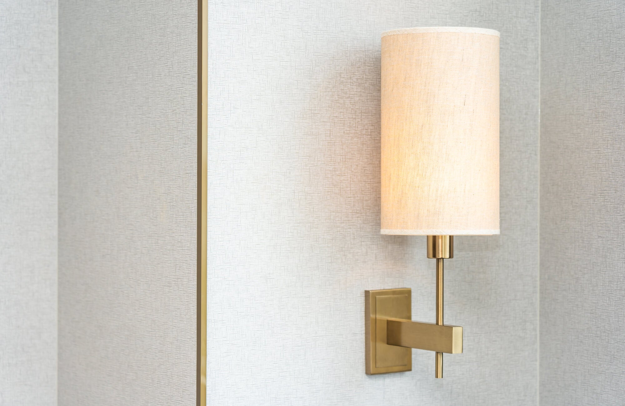 null Close-up of modern wall sconce with brass arm and cylindrical linen shade, mounted on textured neutral wall for soft ambient accent lighting