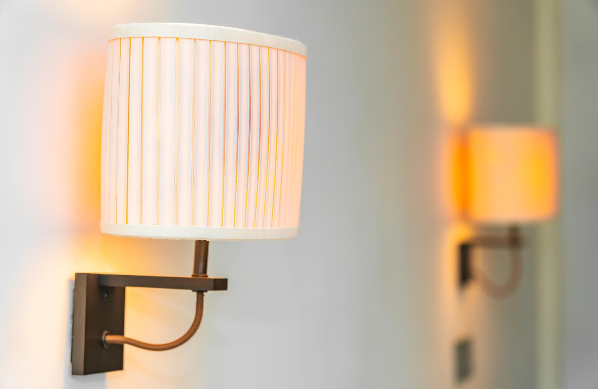 null Contemporary wall sconces with pleated drum shades and bronze arms, casting a soft, warm glow on a clean white wall—ideal for cozy ambient lighting