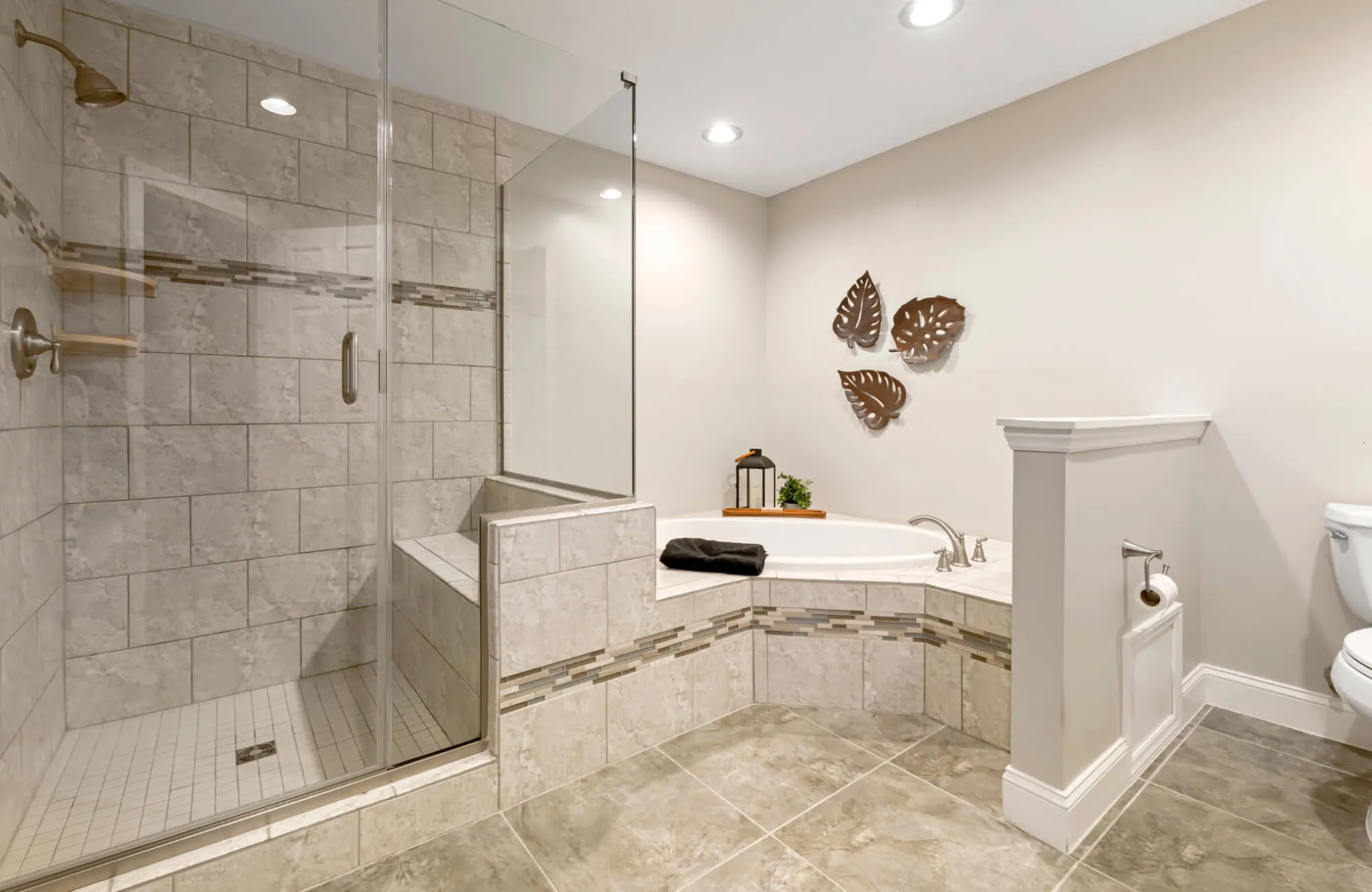 Senior-friendly bathroom with glass-enclosed walk-in shower, built-in tiled bench, and non-slip stone flooring, alongside a soaking tub — spacious design with a low-threshold entry and integrated seating for safer, more accessible bathing.