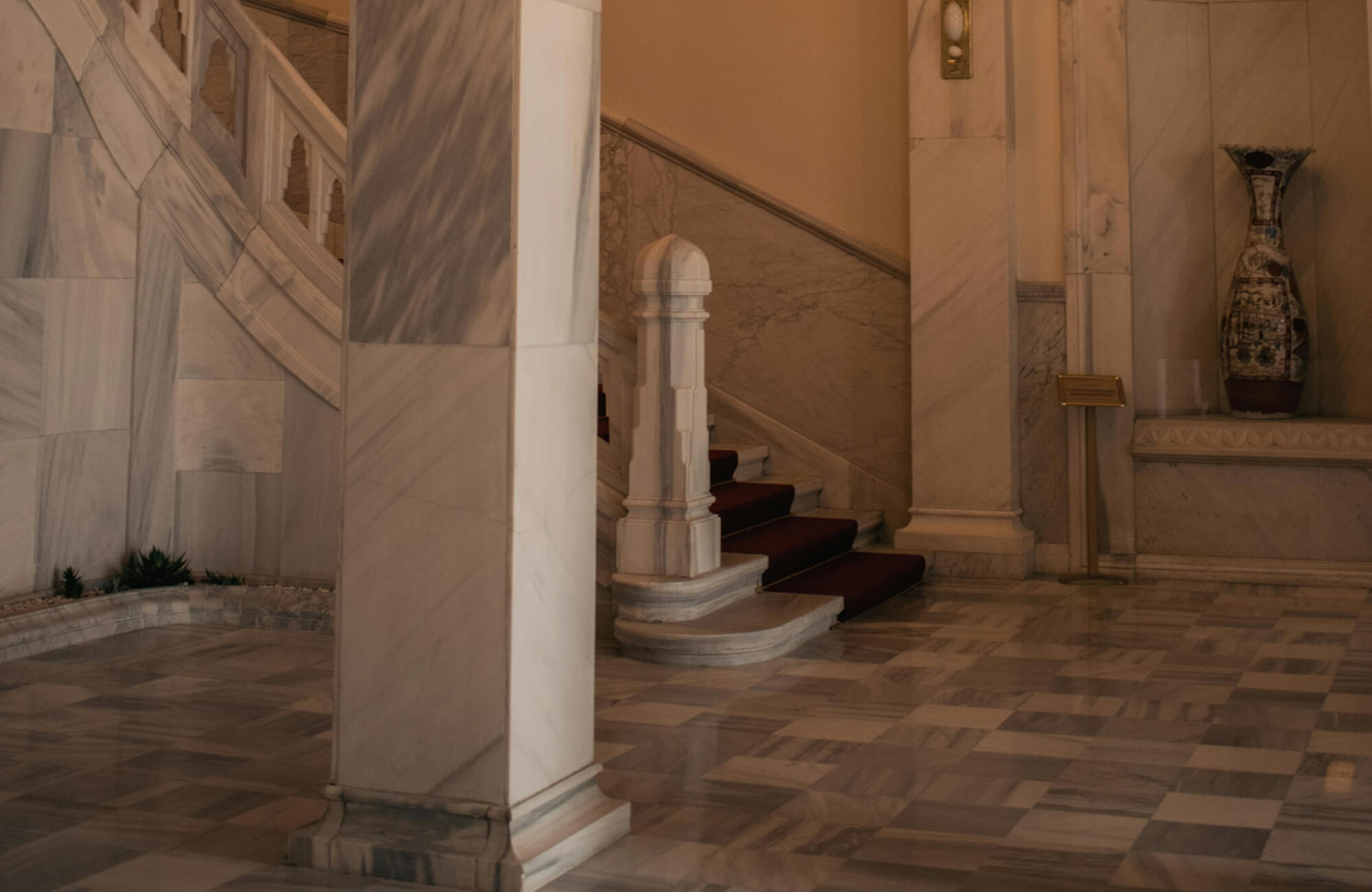 Grand staircase with checkerboard tiles, adorned with marble walls and an intricate vase.