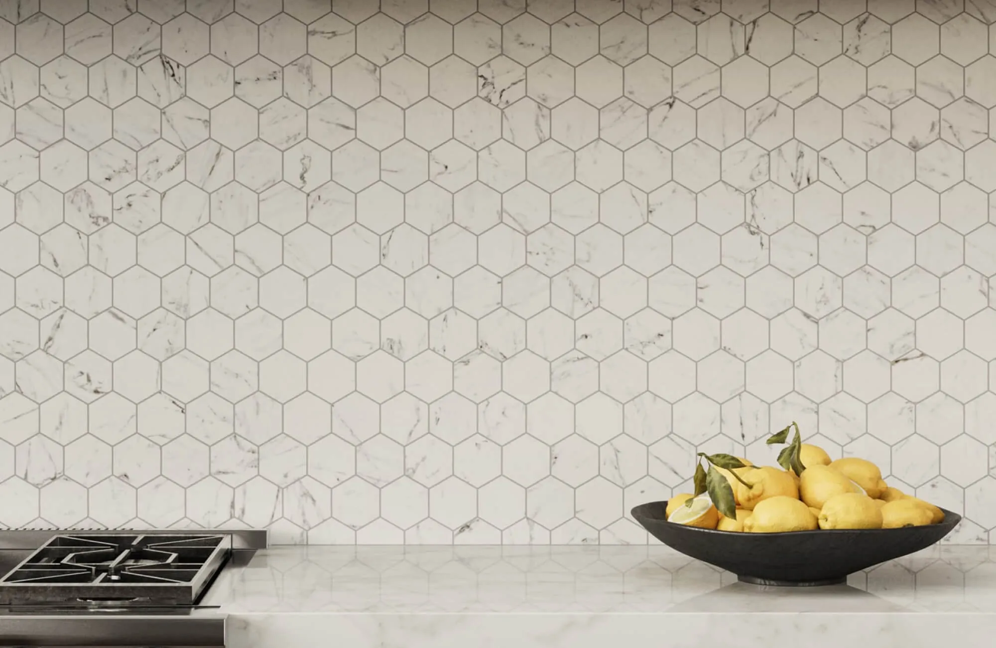 A black fruit bowl filled with lemons on a marble kitchen counter, set against a white hexagon tile backsplash with gray veining.