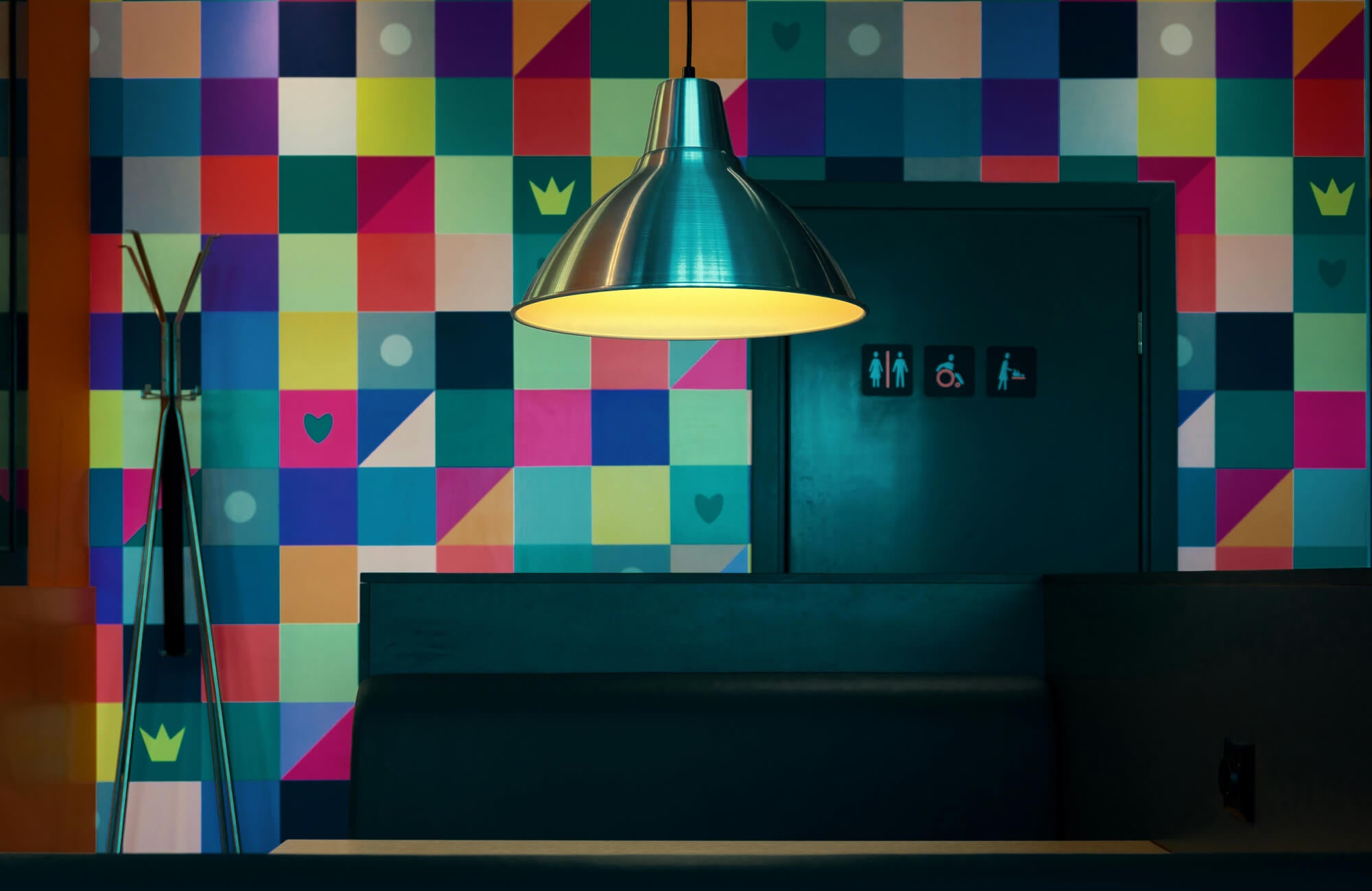 Modern restroom with colorful wallpaper, sleek black seating, pendant light, and modern door signage.