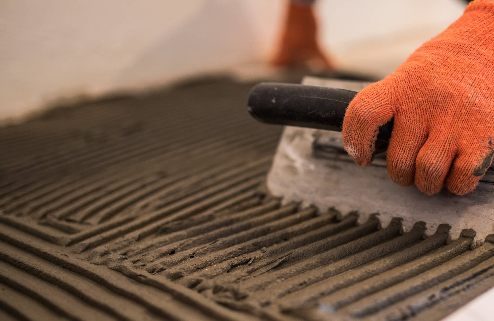 Close-up of a gloved installer spreading thinset mortar with a notched trowel, creating precise ridges essential for proper adhesion and alignment of penny round tile installations.