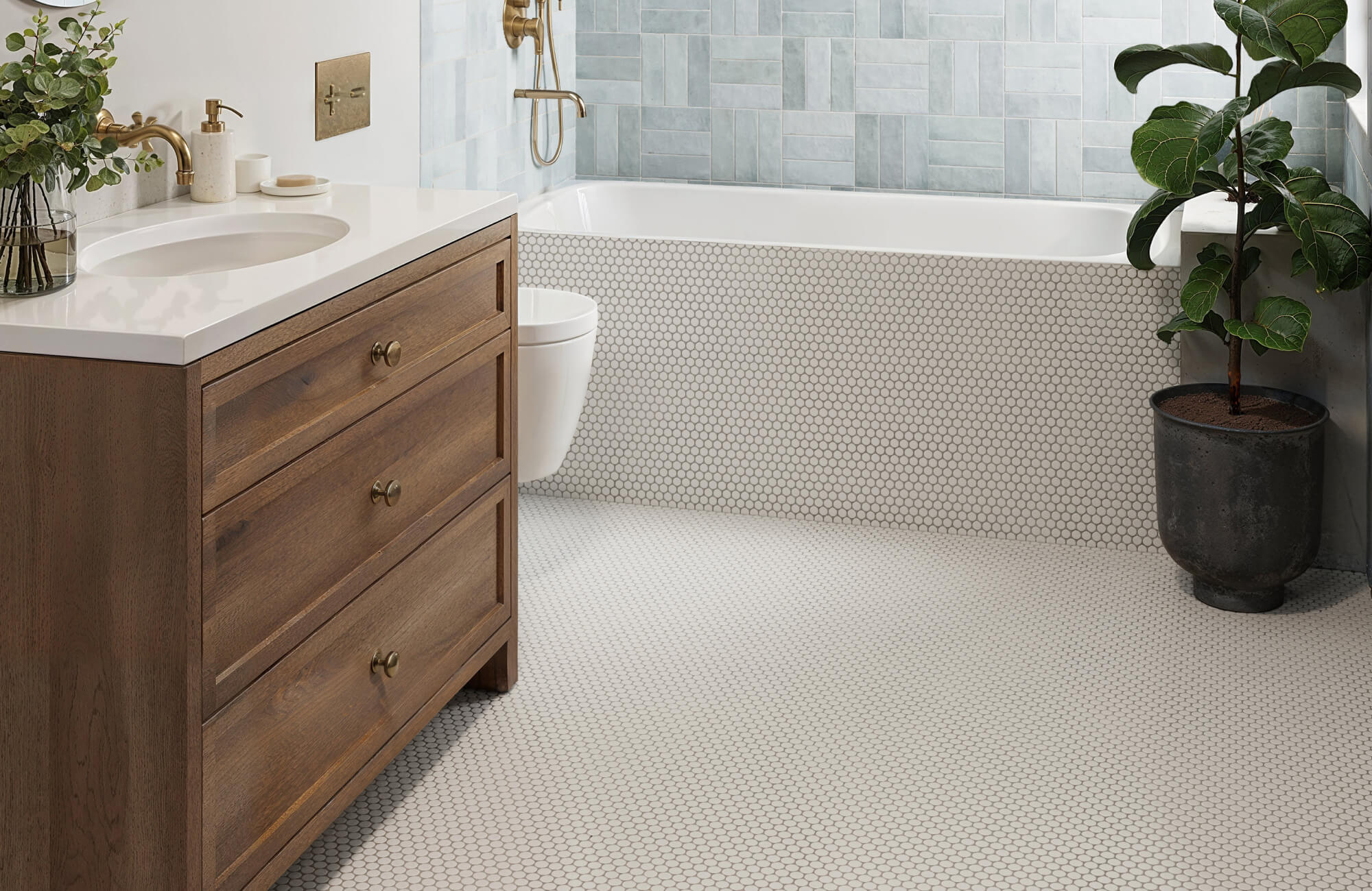 Bright, contemporary bathroom featuring a warm wood vanity, brass fixtures, and a seamless white penny round tile floor and tub surround that add classic texture and a clean, timeless foundation.