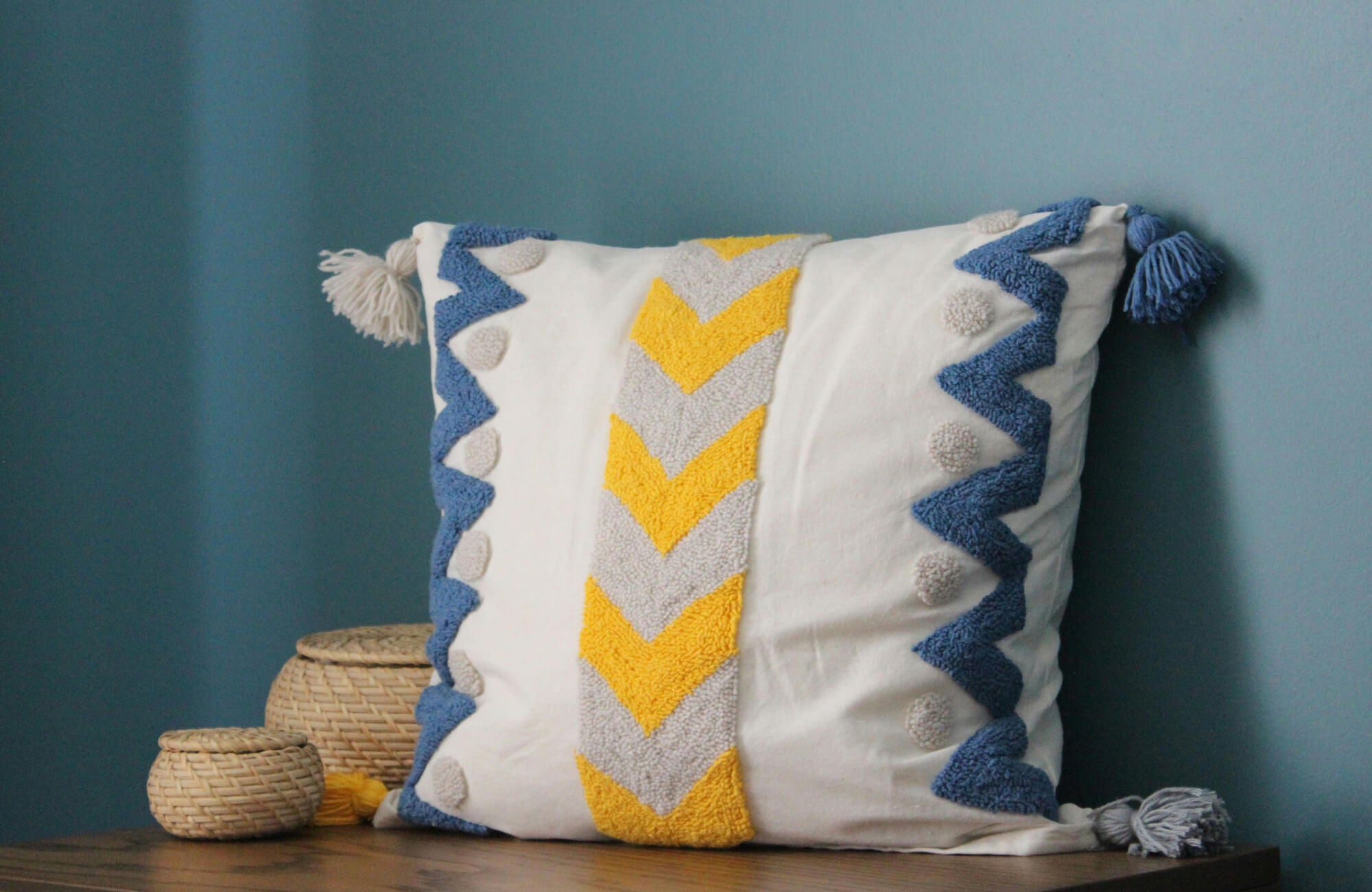 null White decorative pillow with yellow chevron pattern, blue textured trim, and tassel accents.