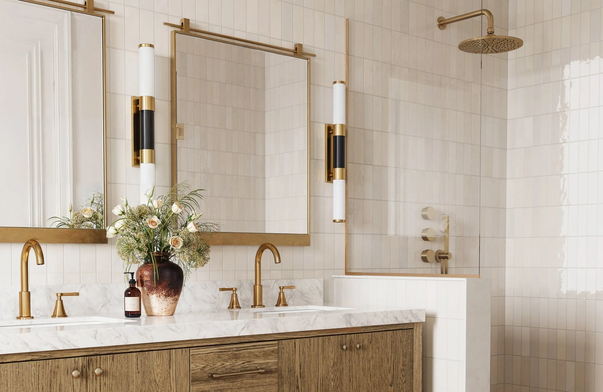 Vertical sconces frame dual mirrors with balanced task lighting in a marble and brass-accented bathroom.